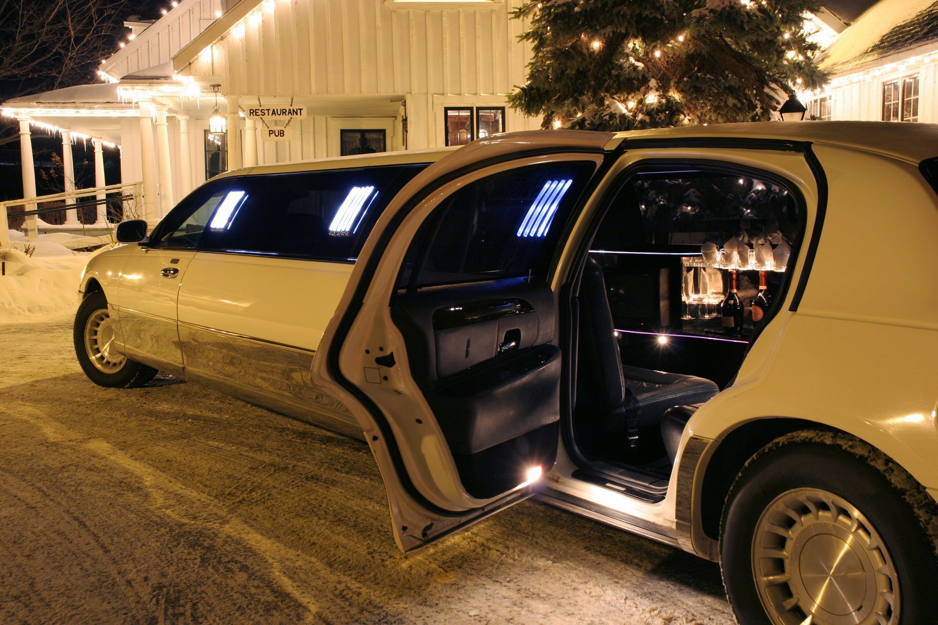 White stretch limousine with open doors and glowing interior parked at night beside a house. White stretch limousine with open doors and glowing interior parked at night beside a house.