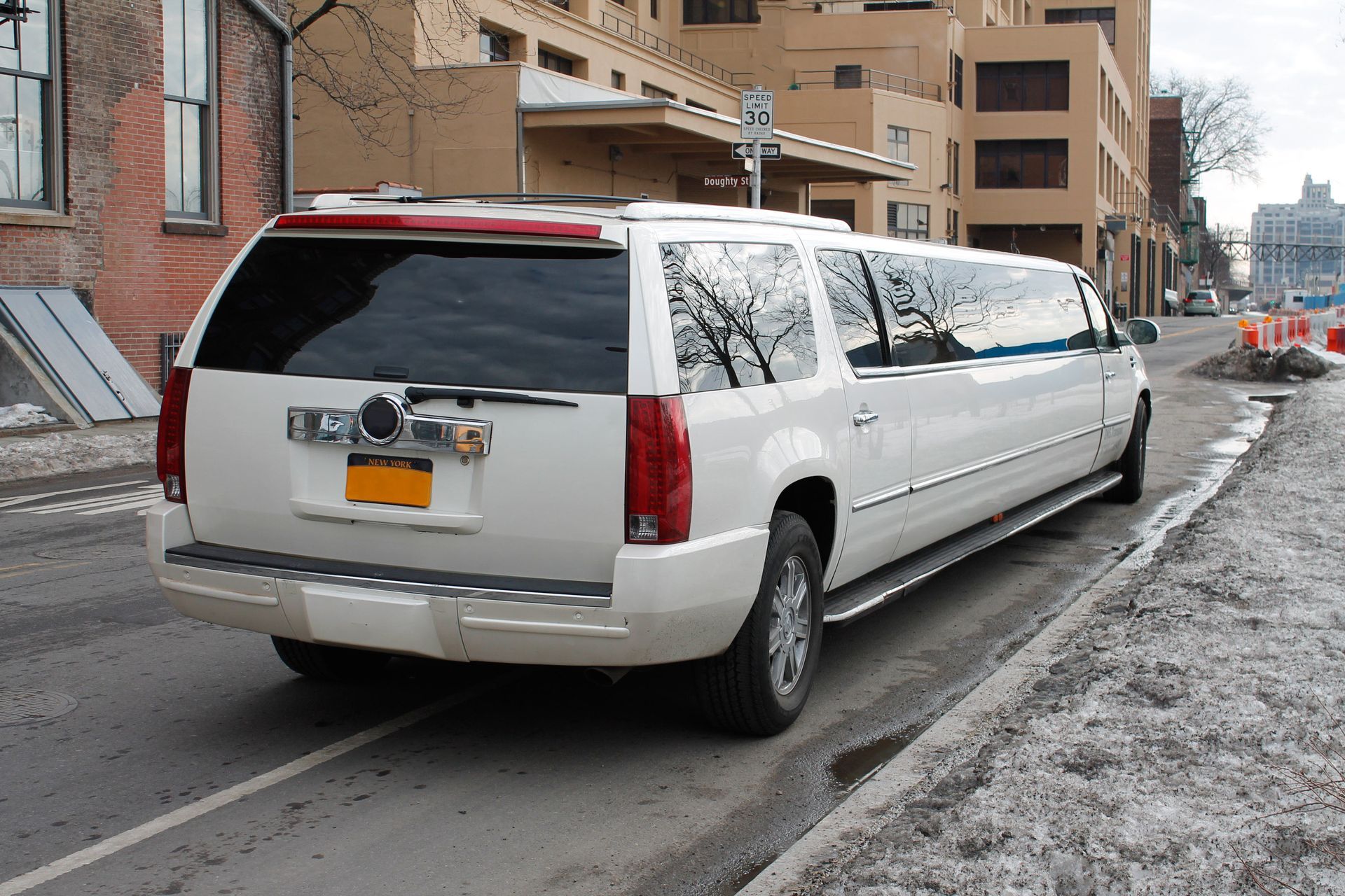 White stretch limousine parked on a snowy city street beside apartment buildings White stretch limousine parked on a snowy city street beside apartment buildings