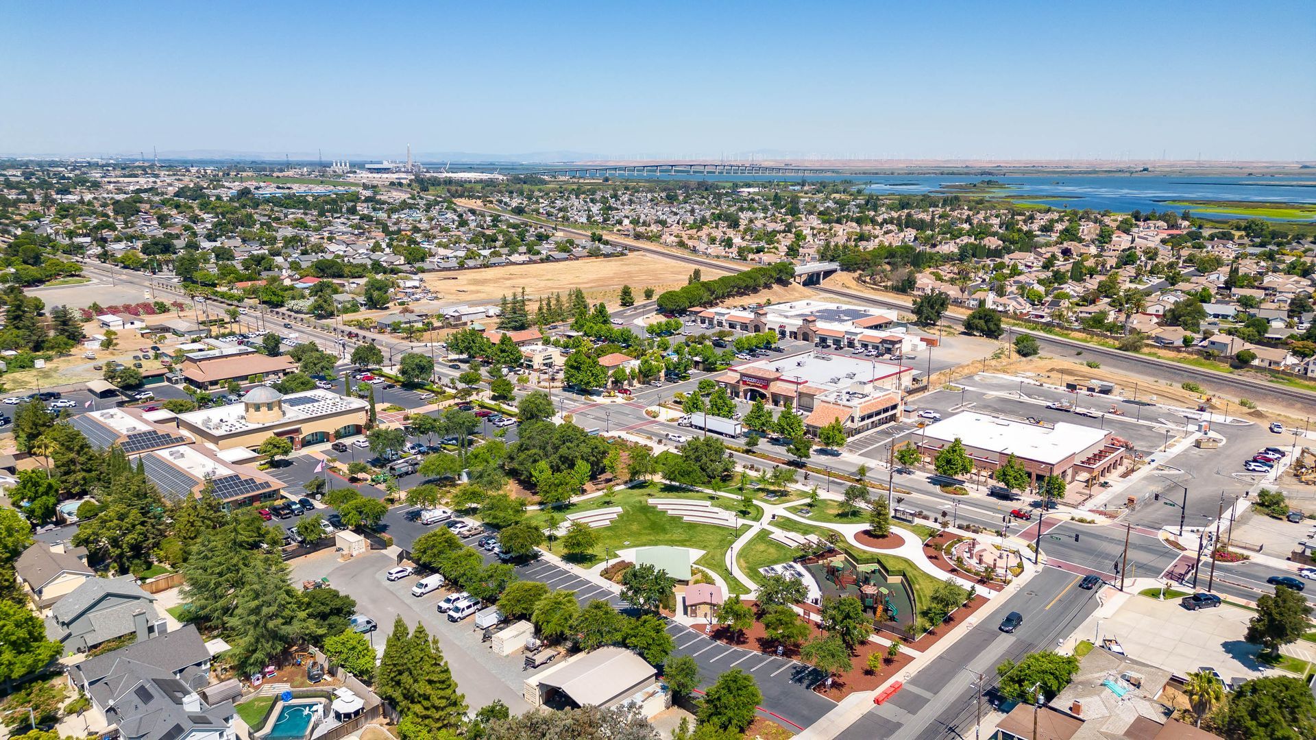 Aerial view of a suburban town center with shops, streets, parking lots, and palm-lined neighborhoods under a clear sky