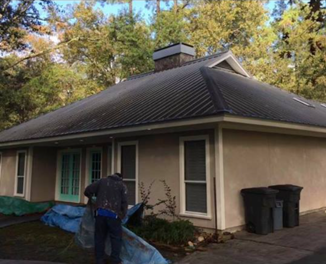 Worker arranging a blue tarp beside shrubs at a home with a metal roof