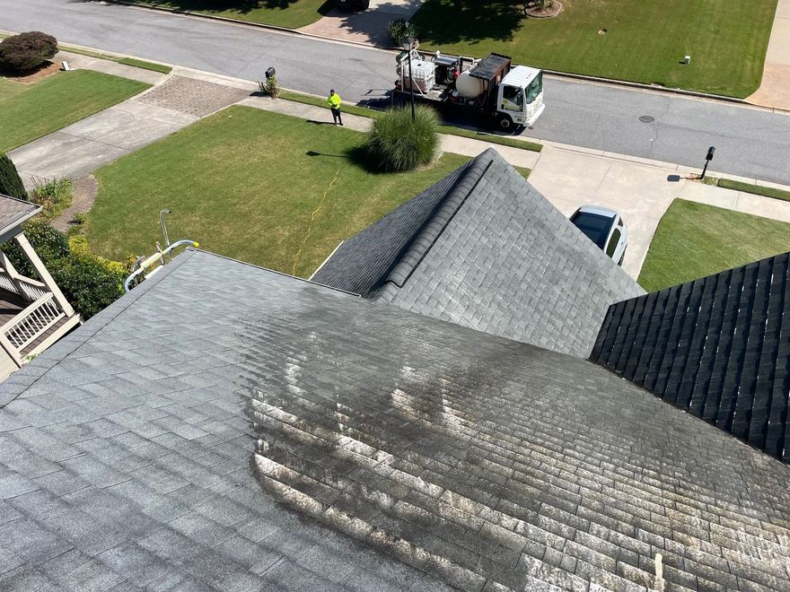 Residential asphalt shingle roof with cleaning equipment parked on the street