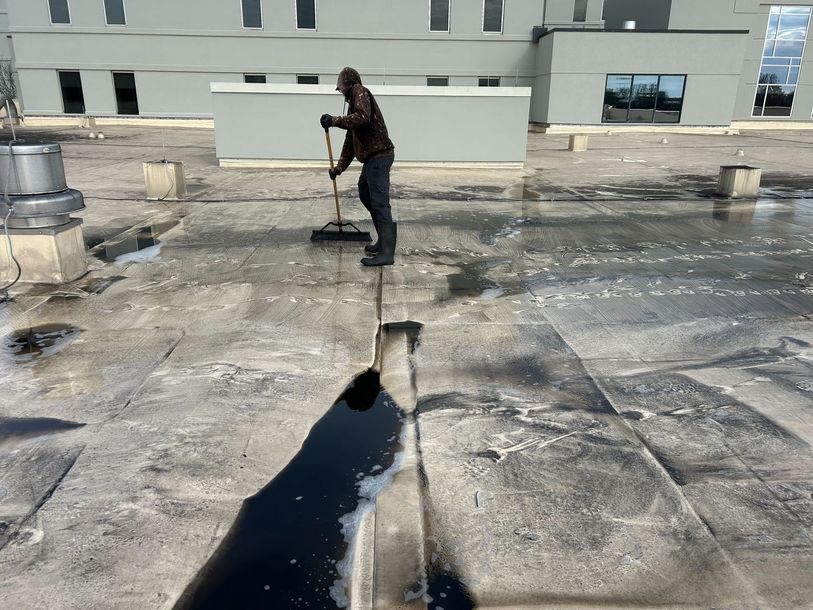 Worker brushing a wet flat commercial roof near rooftop vents