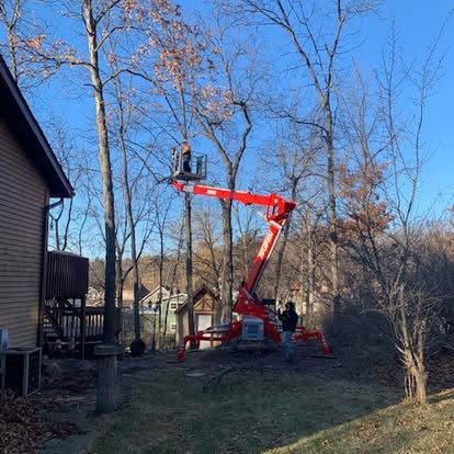 Bucket lift raised into bare tree branches beside a home for tree trimming