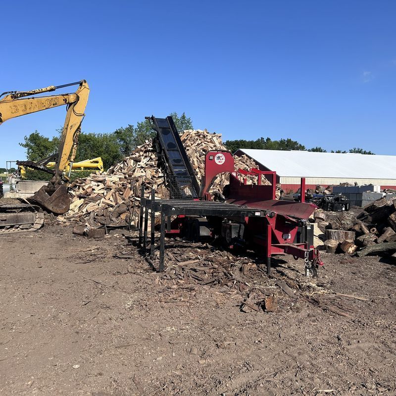 Excavator loading firewood processing equipment with wood debris