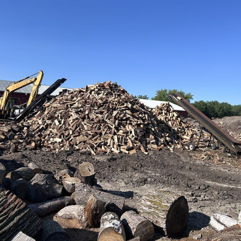 Excavator moving material next to a large firewood chip pile