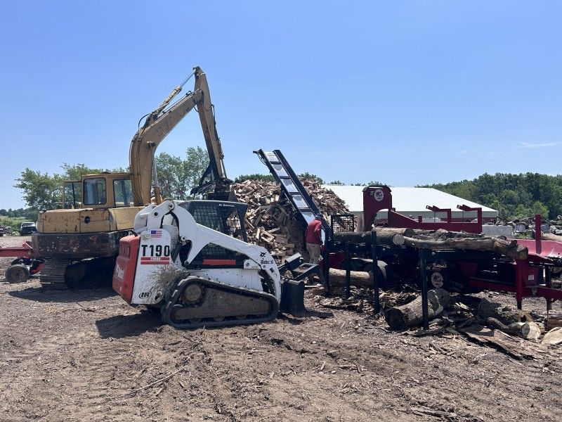 Skid steer loading wood debris onto firewood processing equipment in Kenosha, WI