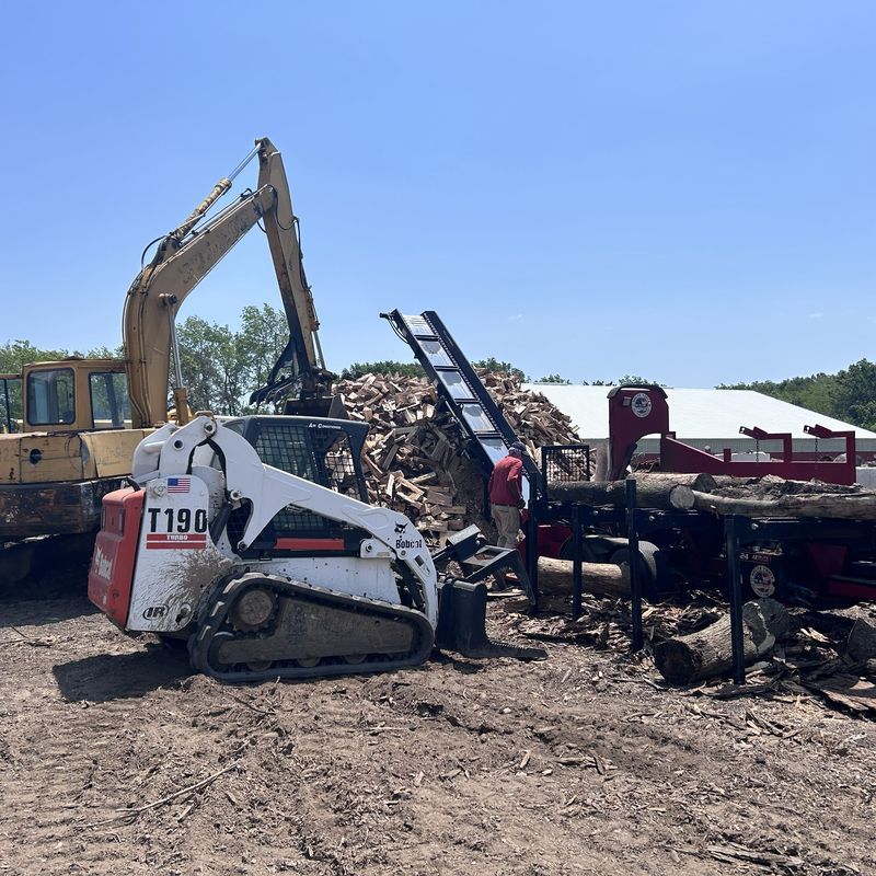 Excavator loading firewood processing equipment with wood debris in Kenosha, WI