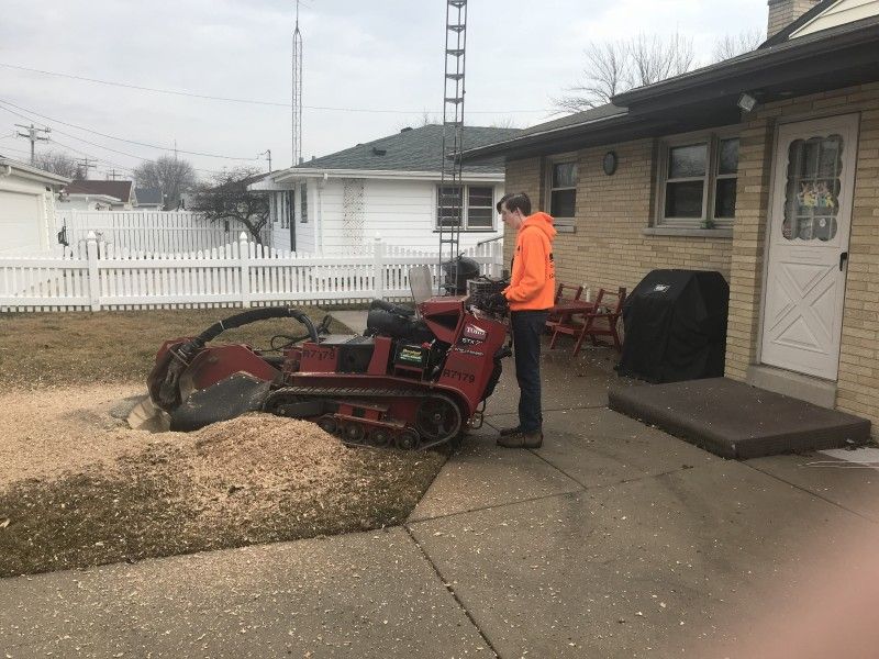 Stump grinder parked in a yard near a home's porch, Haas Tree Service