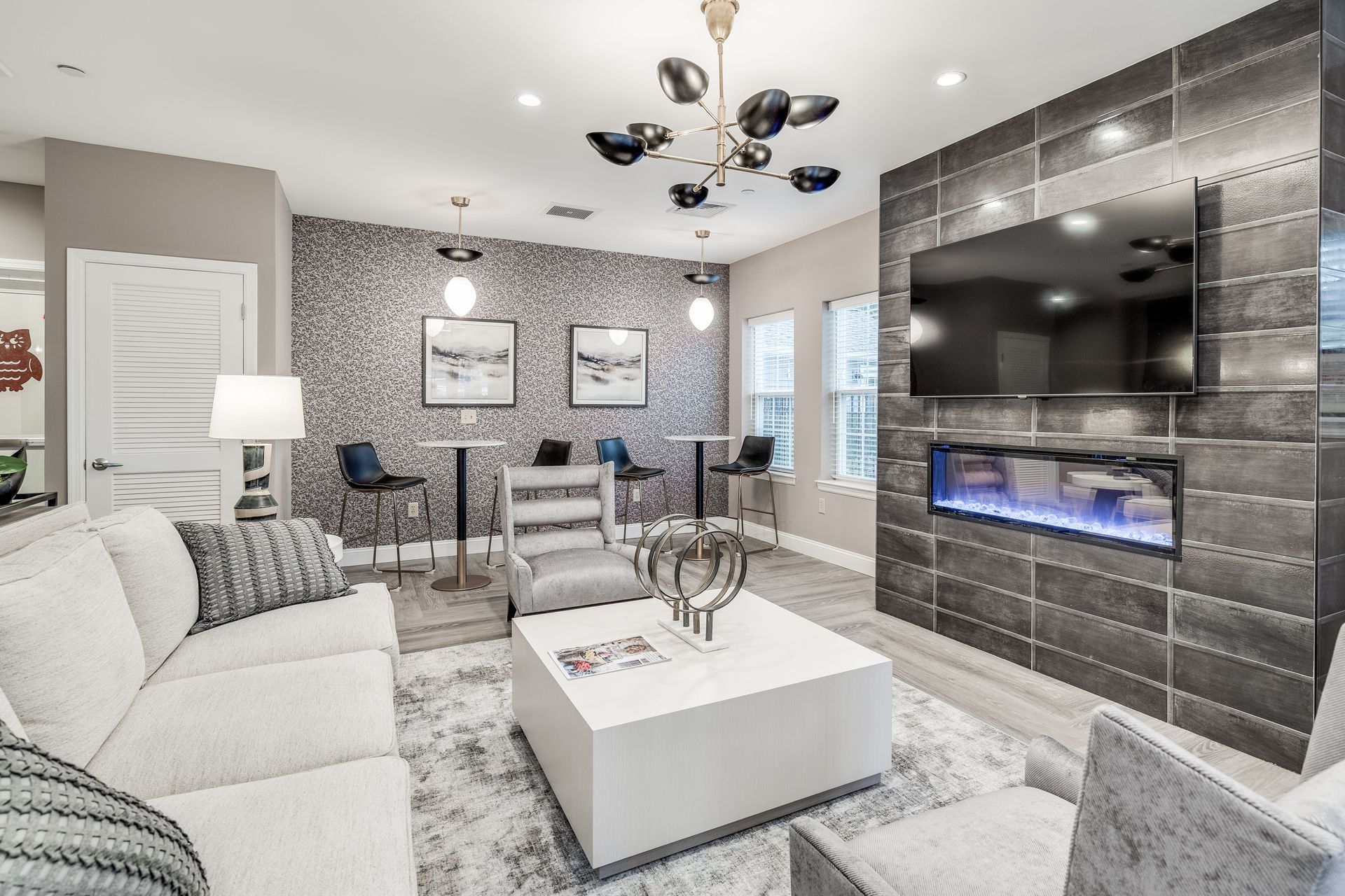 Lounge with a white couch, fireplace, TV, and decorative chandelier in a modern building.