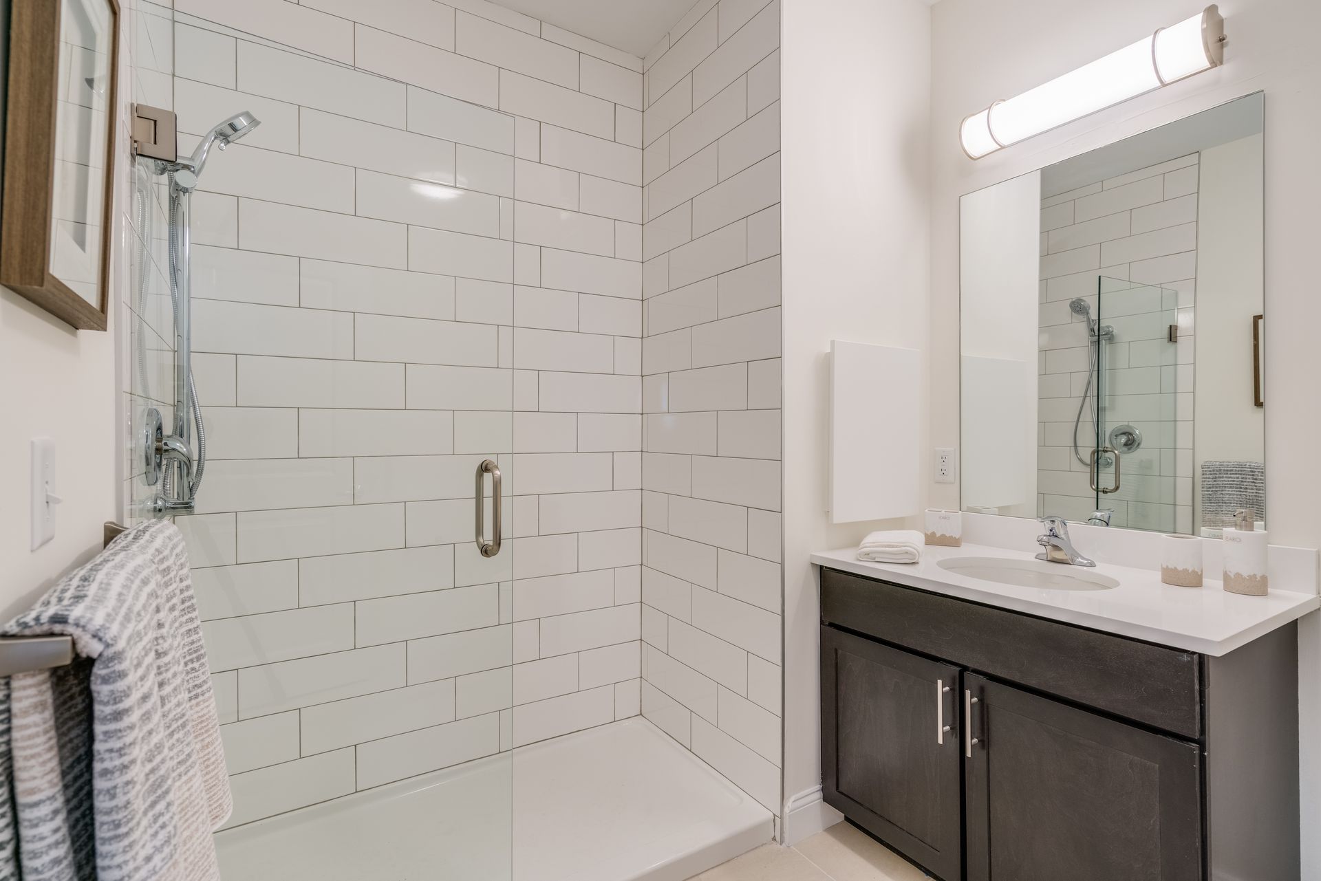 Bathroom with a white tiled shower, glass door, vanity with dark cabinets, and a large mirror.