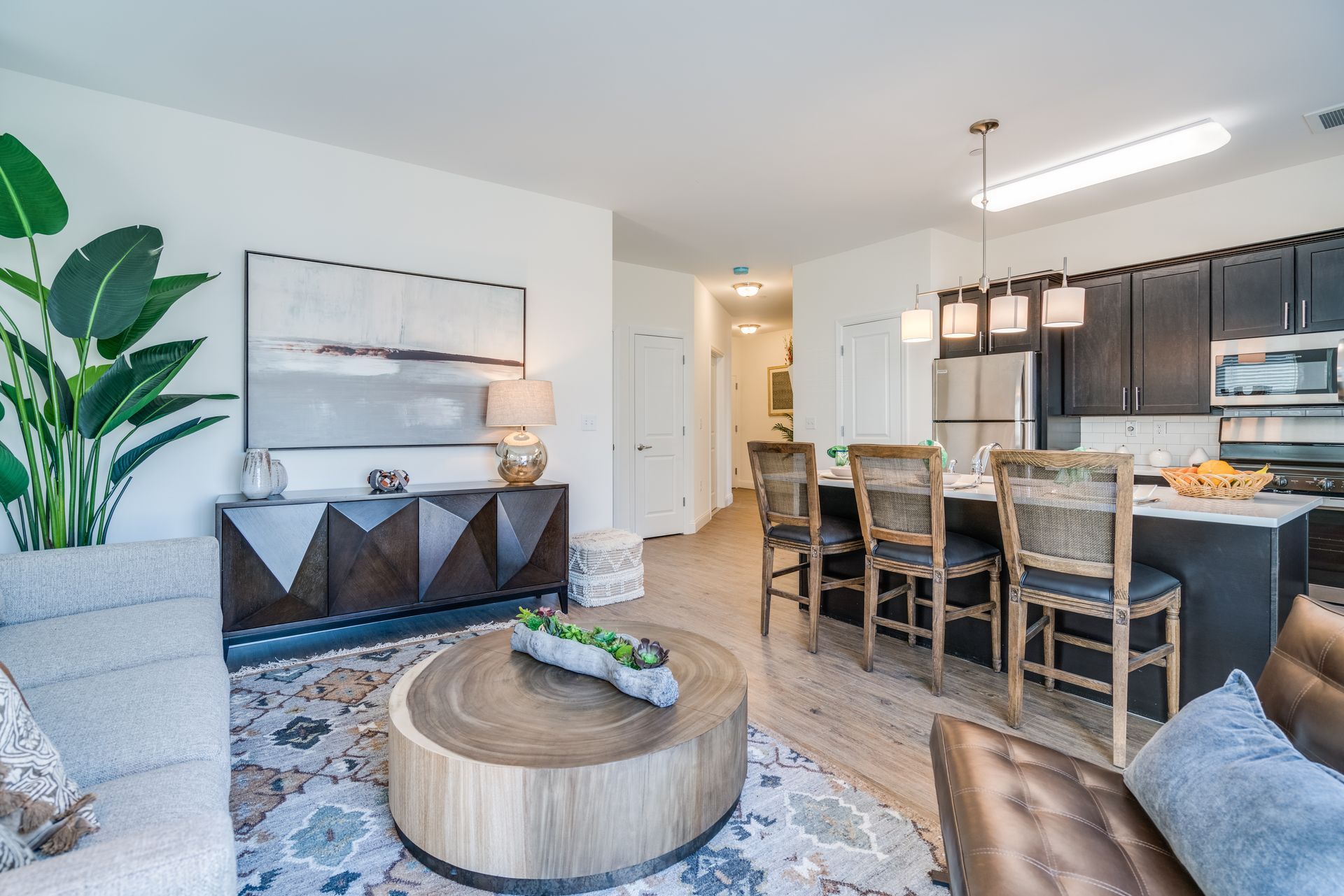 Living room with kitchen in background; sofa, coffee table, kitchen island with bar stools, and decorative elements.