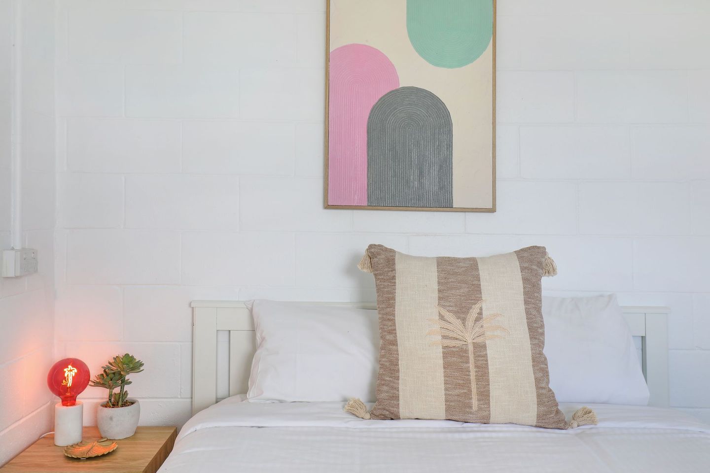 A bed with a pillow and a painting on the wall above it.