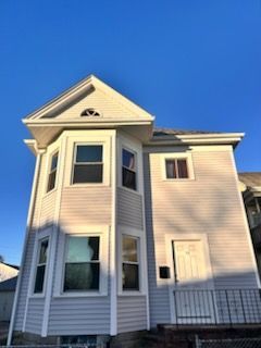 Two-story beige house with white trim and a front porch under a blue sky