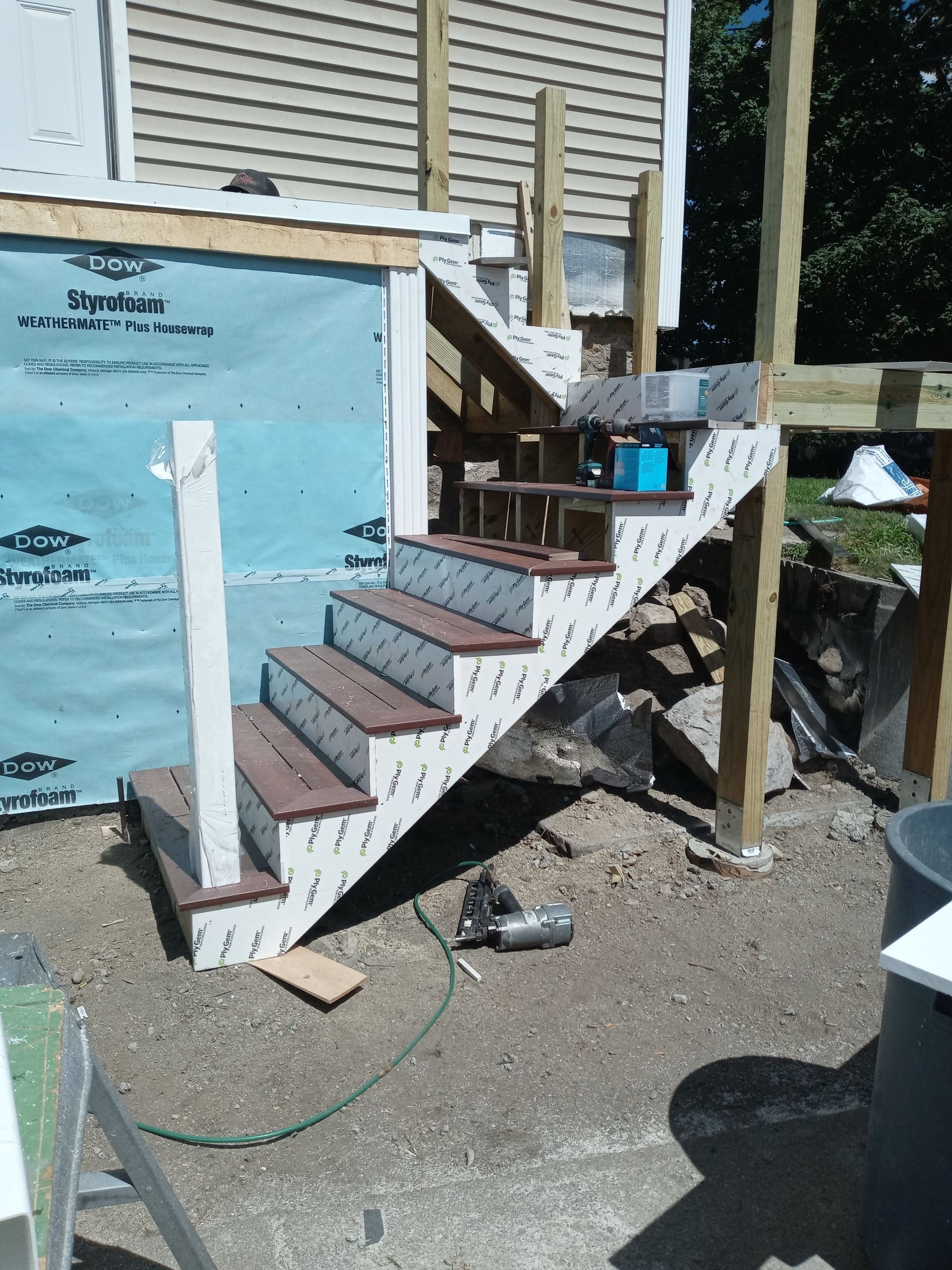 Outdoor wooden stairs under construction beside a house, with exposed framing and blue sheathing.