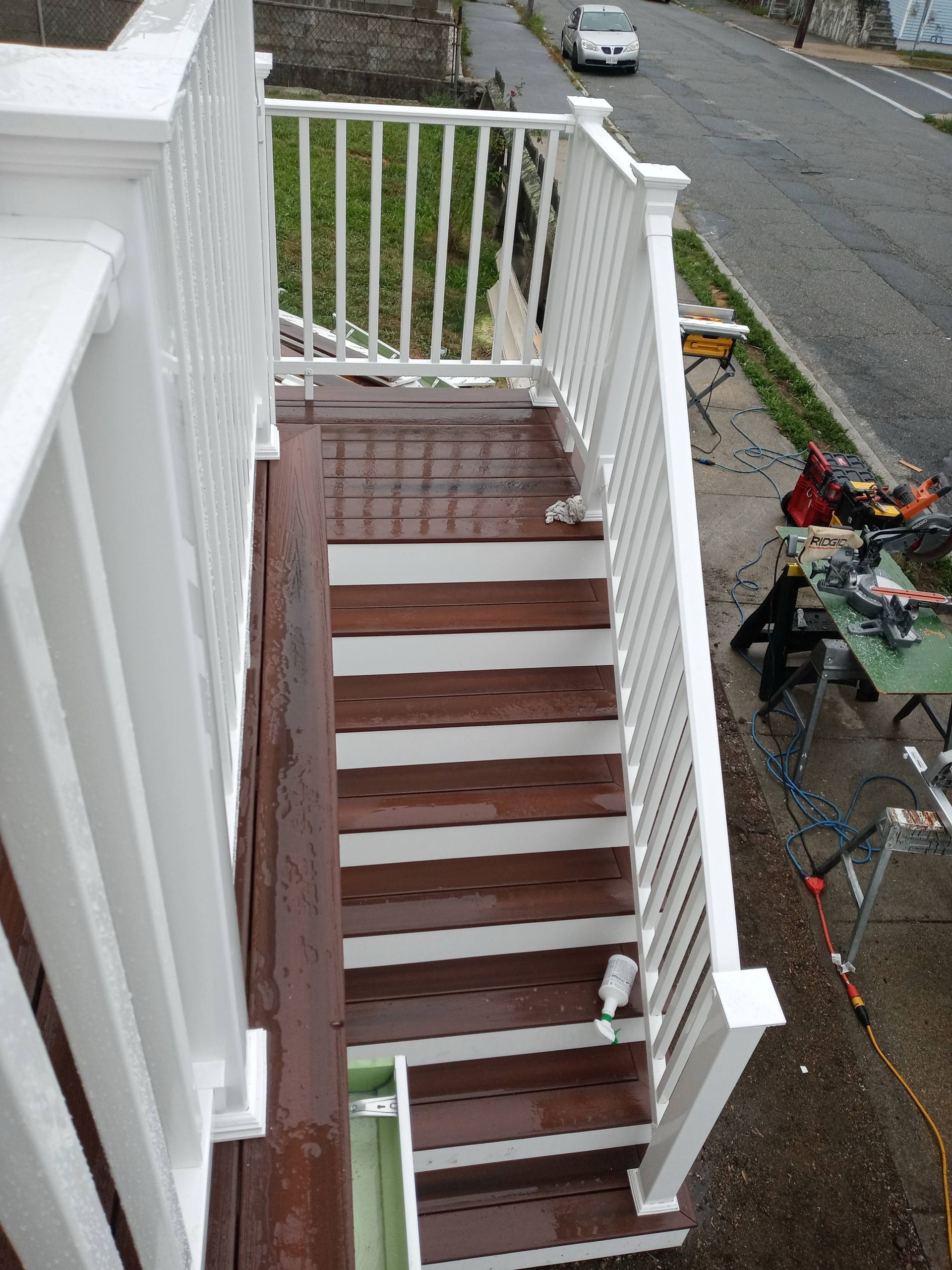 Narrow outdoor stairway with white railings and brown steps beside a street and sidewalk clutter