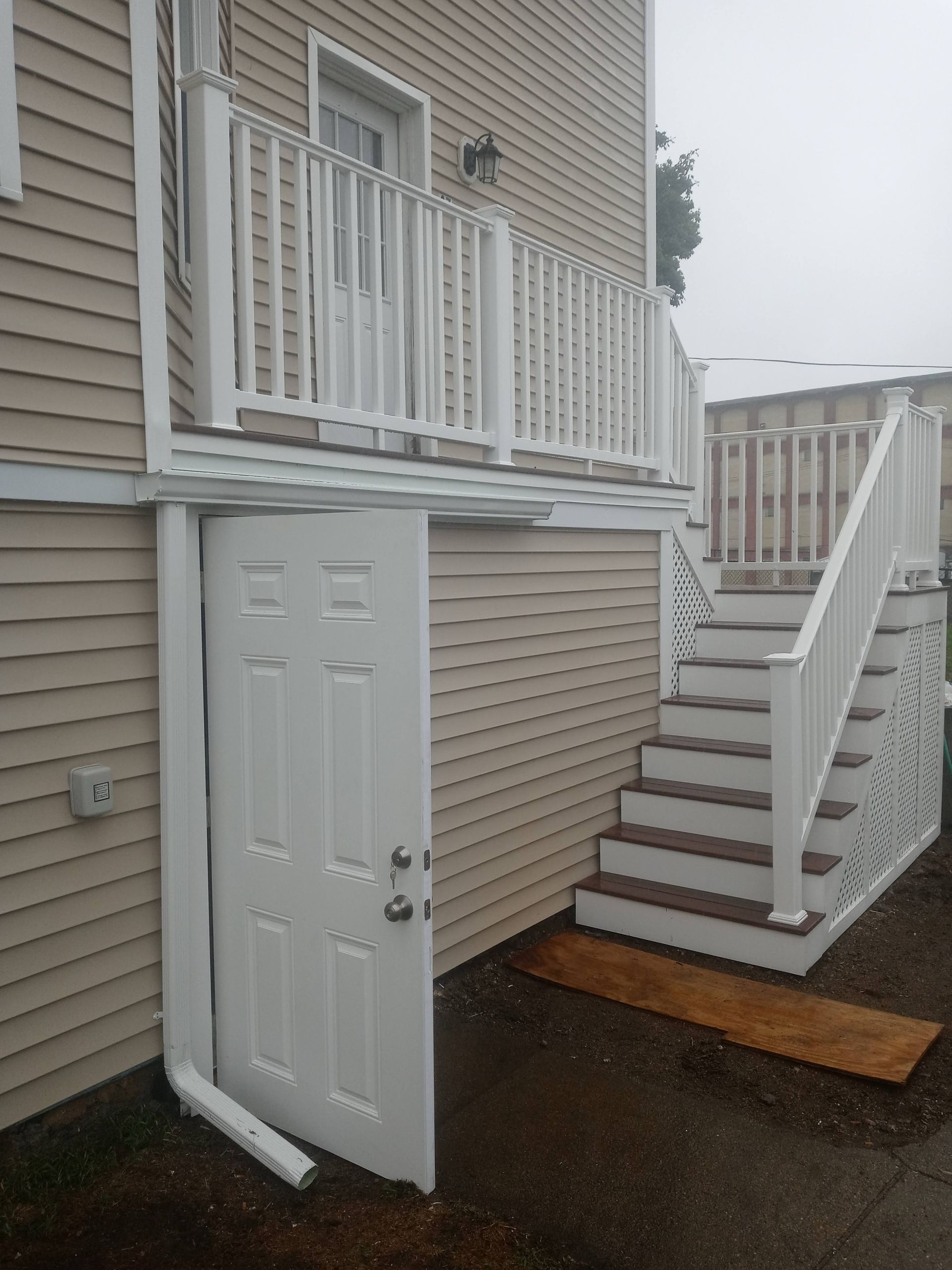 Open exterior door beneath a balcony beside a wet staircase in a beige townhouse courtyard
