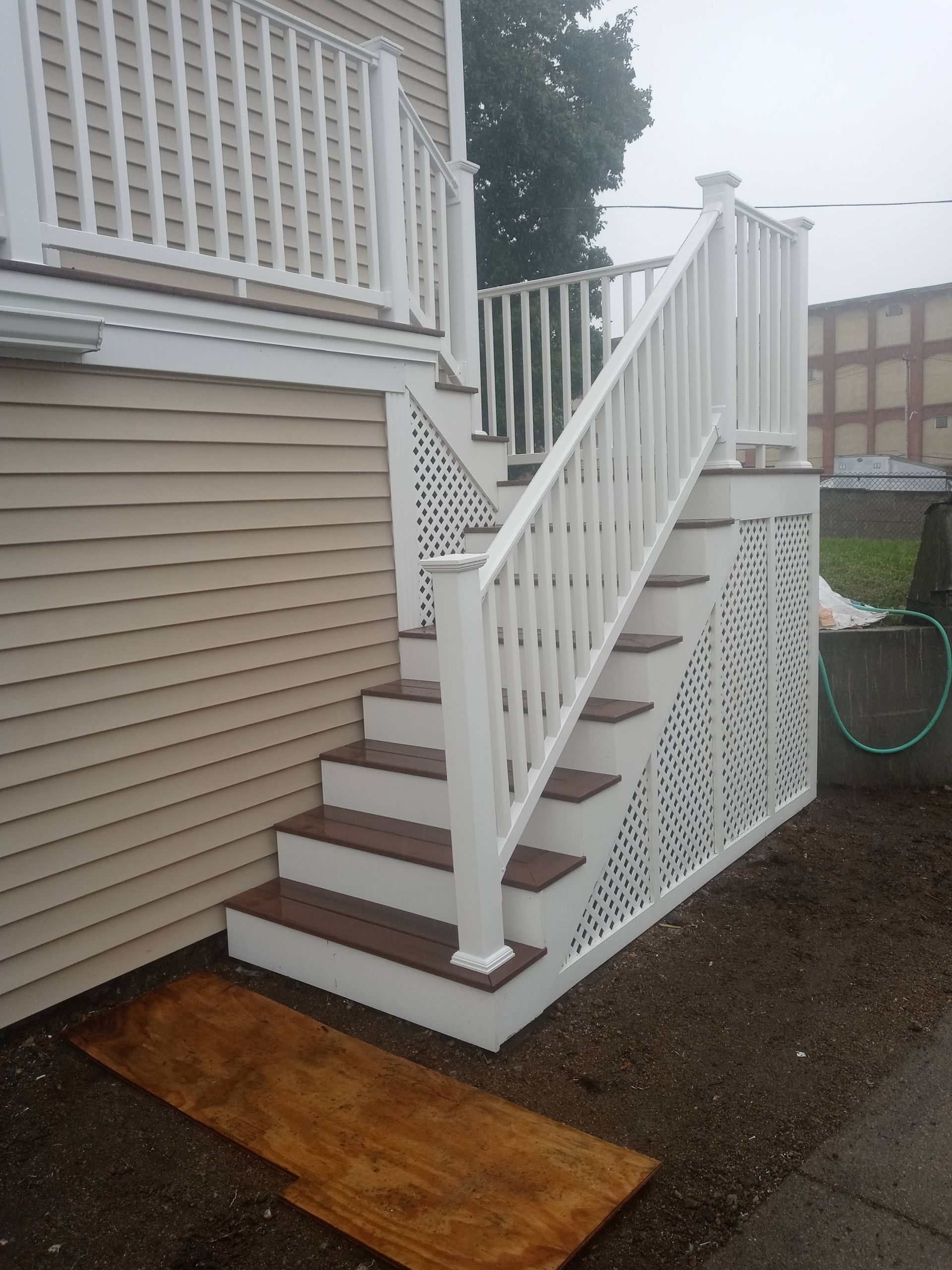 Exterior stairs with a white handrail and lattice ramp beside a beige house