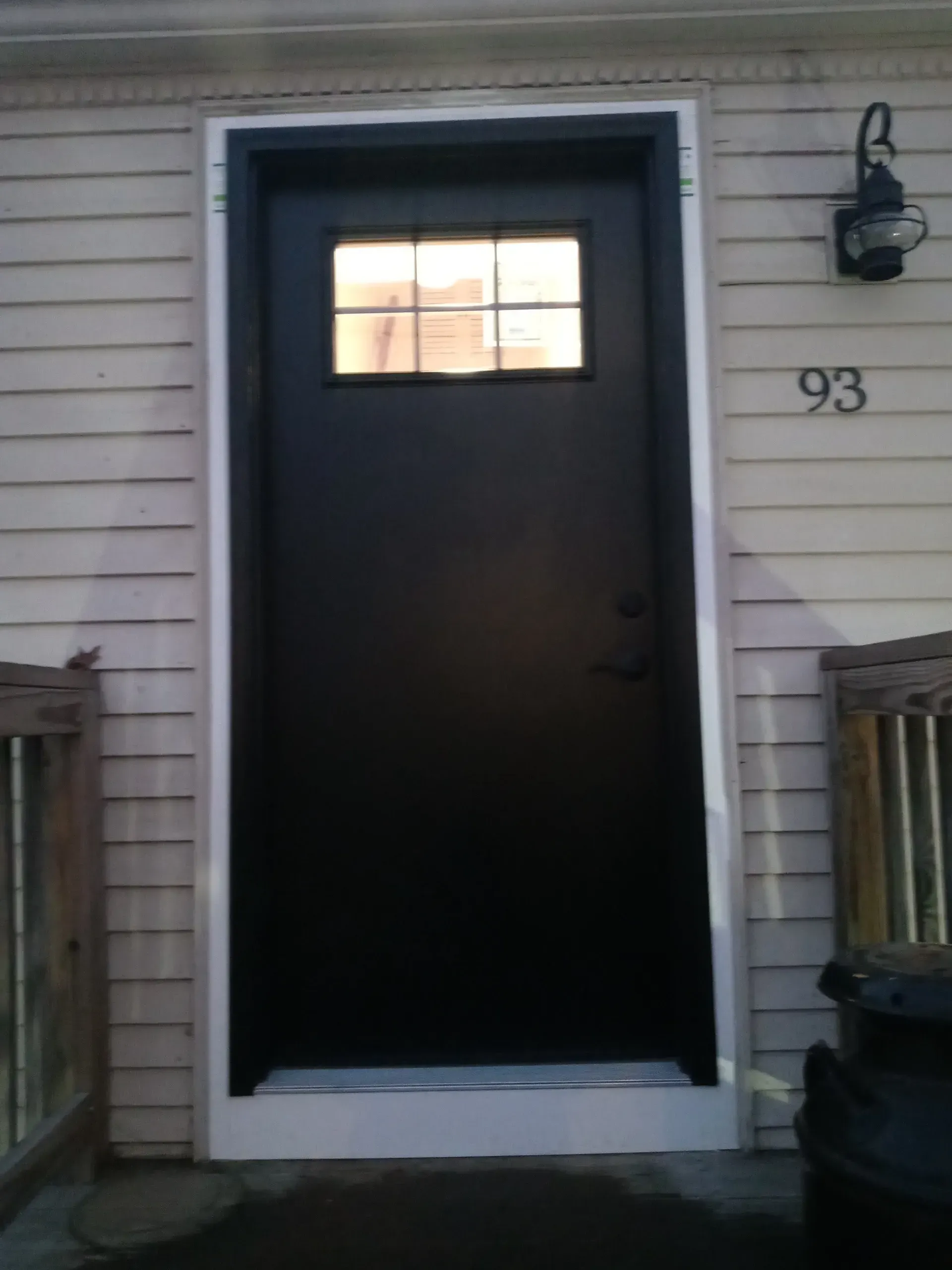 Front door of a house with a lit window panel and house number 93 beside it.