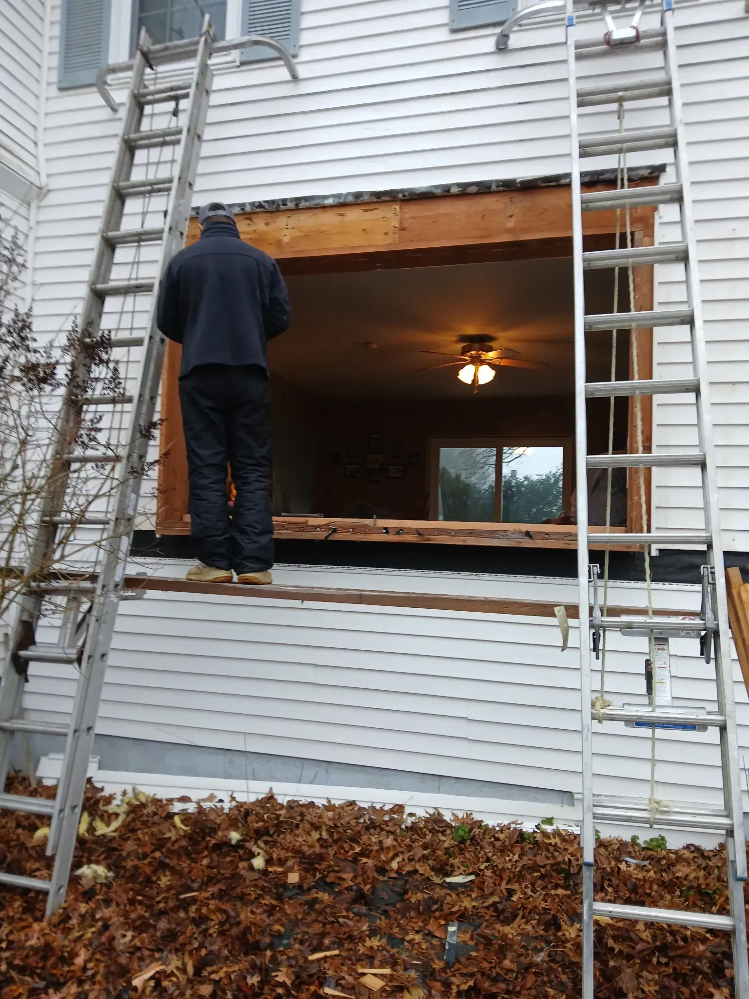 Worker on a ladder repairing a house exterior window opening with siding removed