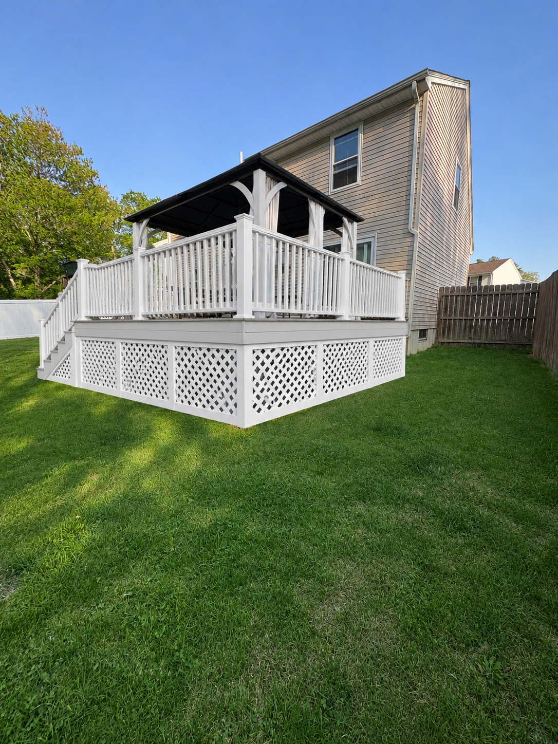 White wooden deck and gazebo attached to a brick house on a green lawn