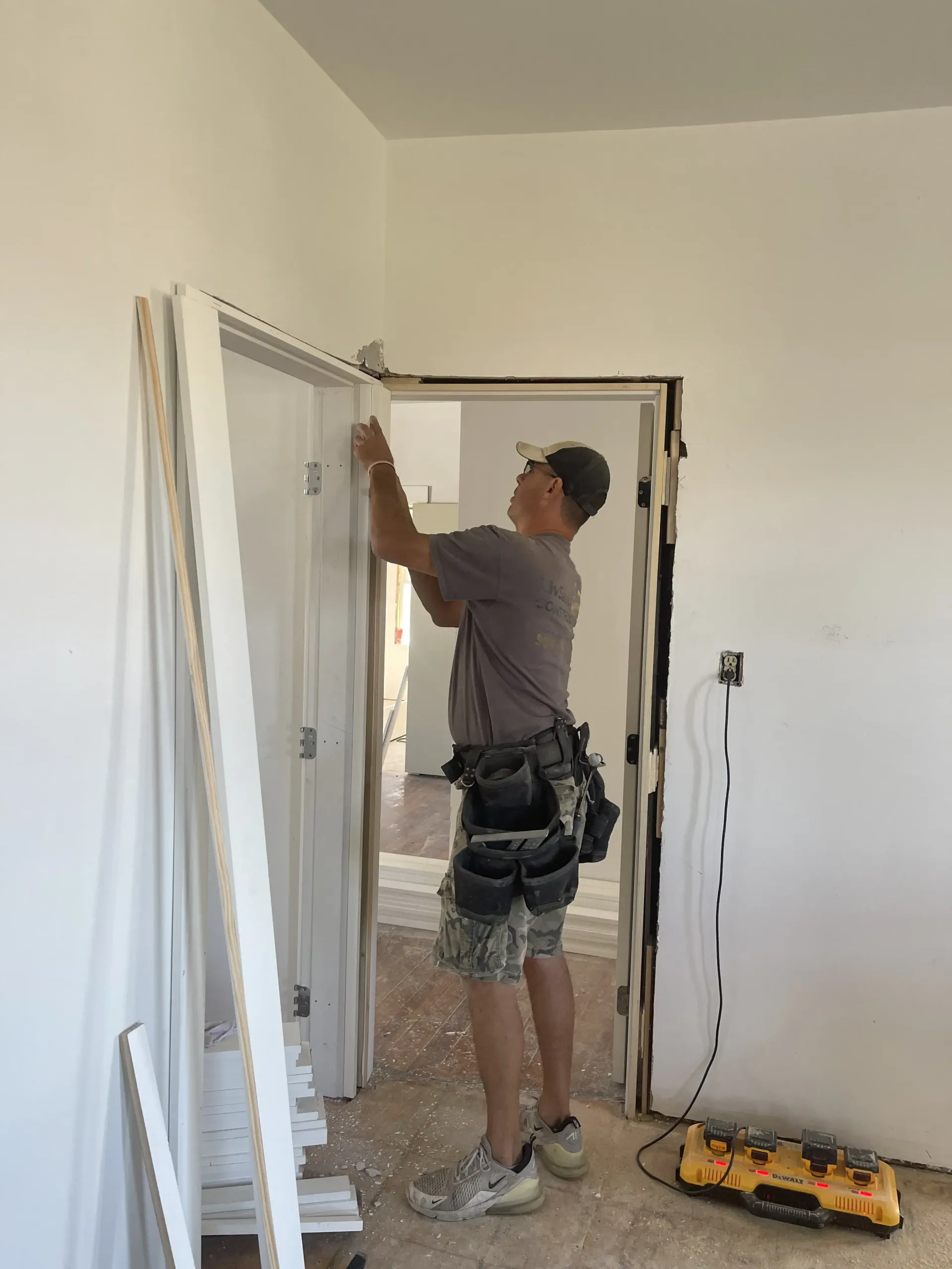 Worker installing a white door frame in an unfinished room, with tools on the floor.