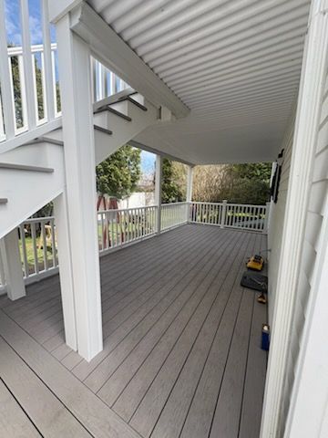 Covered porch with gray decking, white railings, and stairs leading down to a yard.