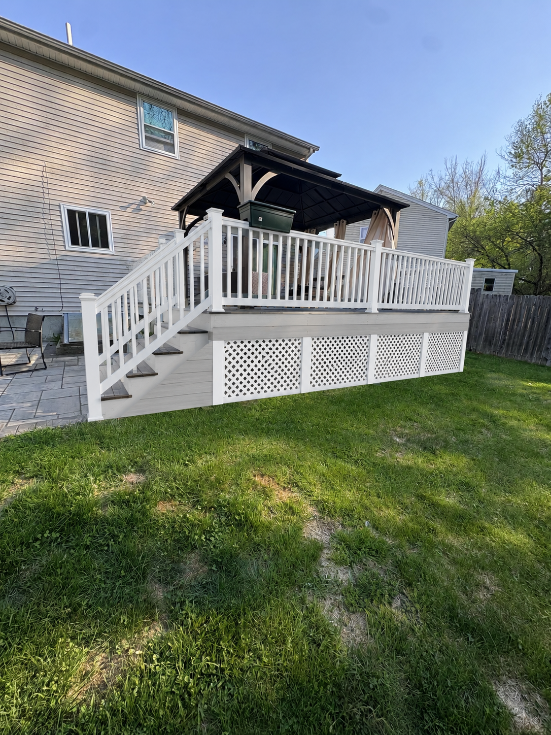 White deck with stairs and railing attached to a house in a grassy backyard
