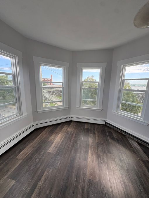 Bright empty room with bay windows, white walls, and dark wood flooring.