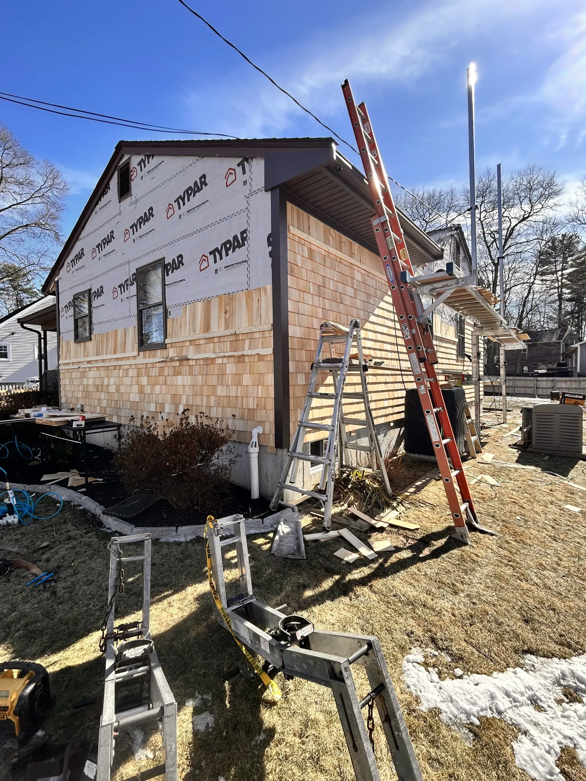 Damaged house exterior with debris, ladders, and exposed insulation after storm or construction work