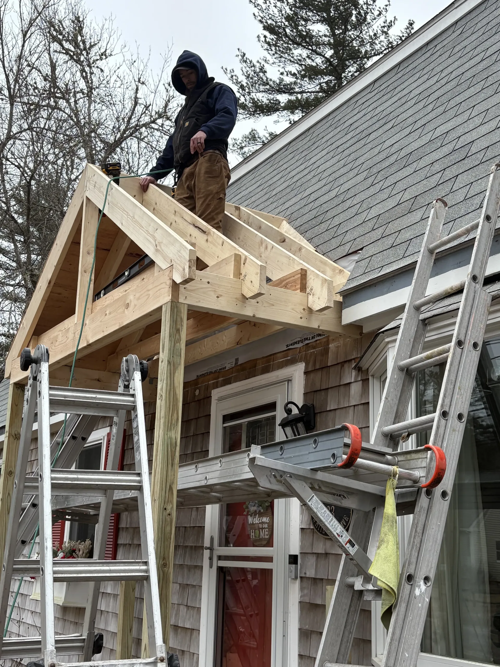 Worker on ladders framing a wooden roof over a brick house exterior