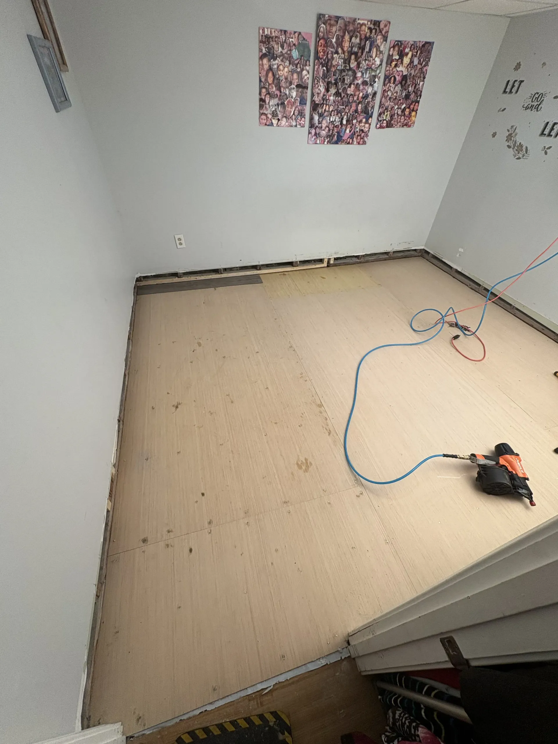 Empty room with new flooring being installed, tools and cord on the floor, wall photos in the background