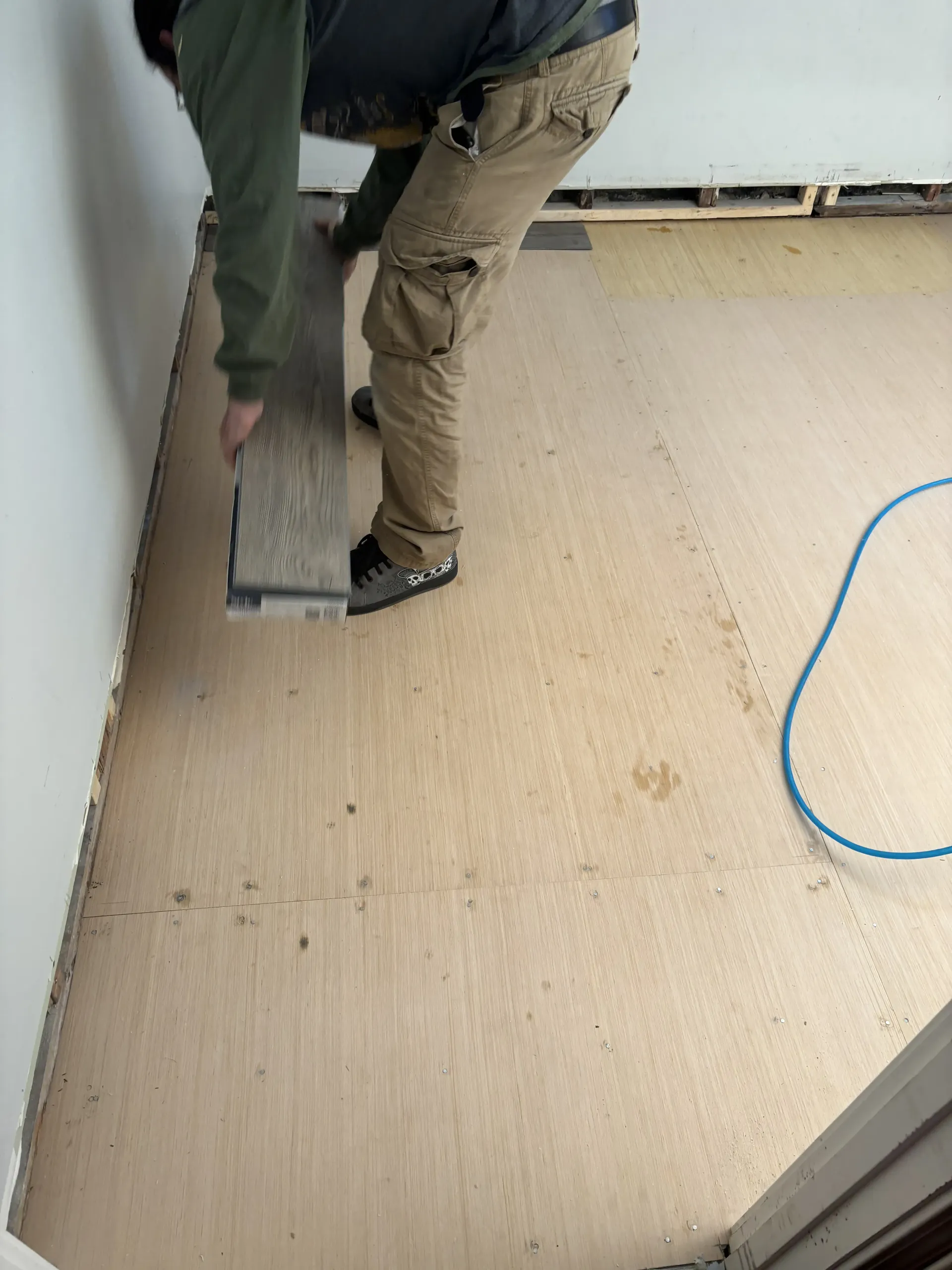 Two workers installing beige flooring in a room, with a blue cable on the floor.
