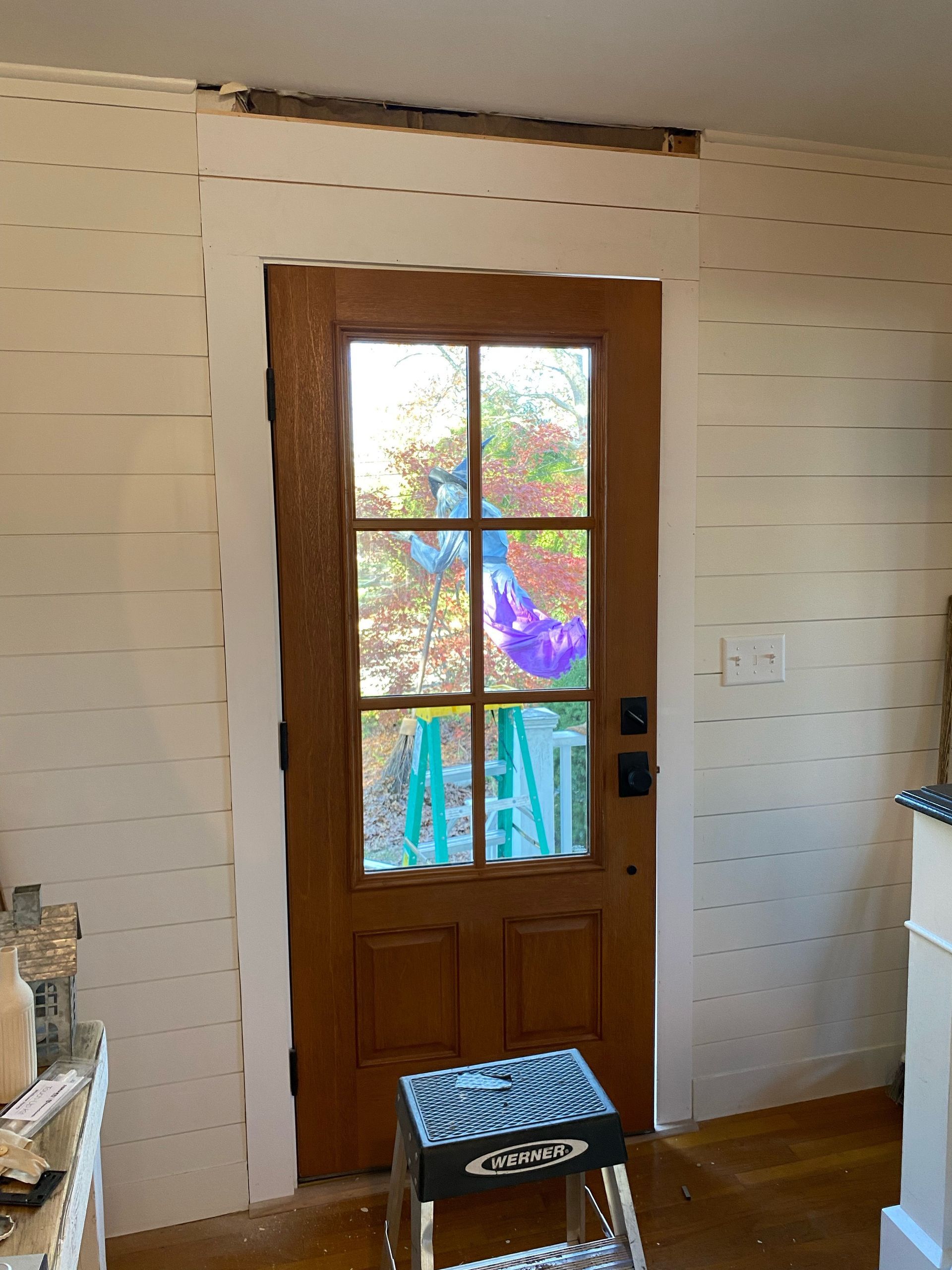 Wooden front door with stained glass panels in a white-paneled hallway