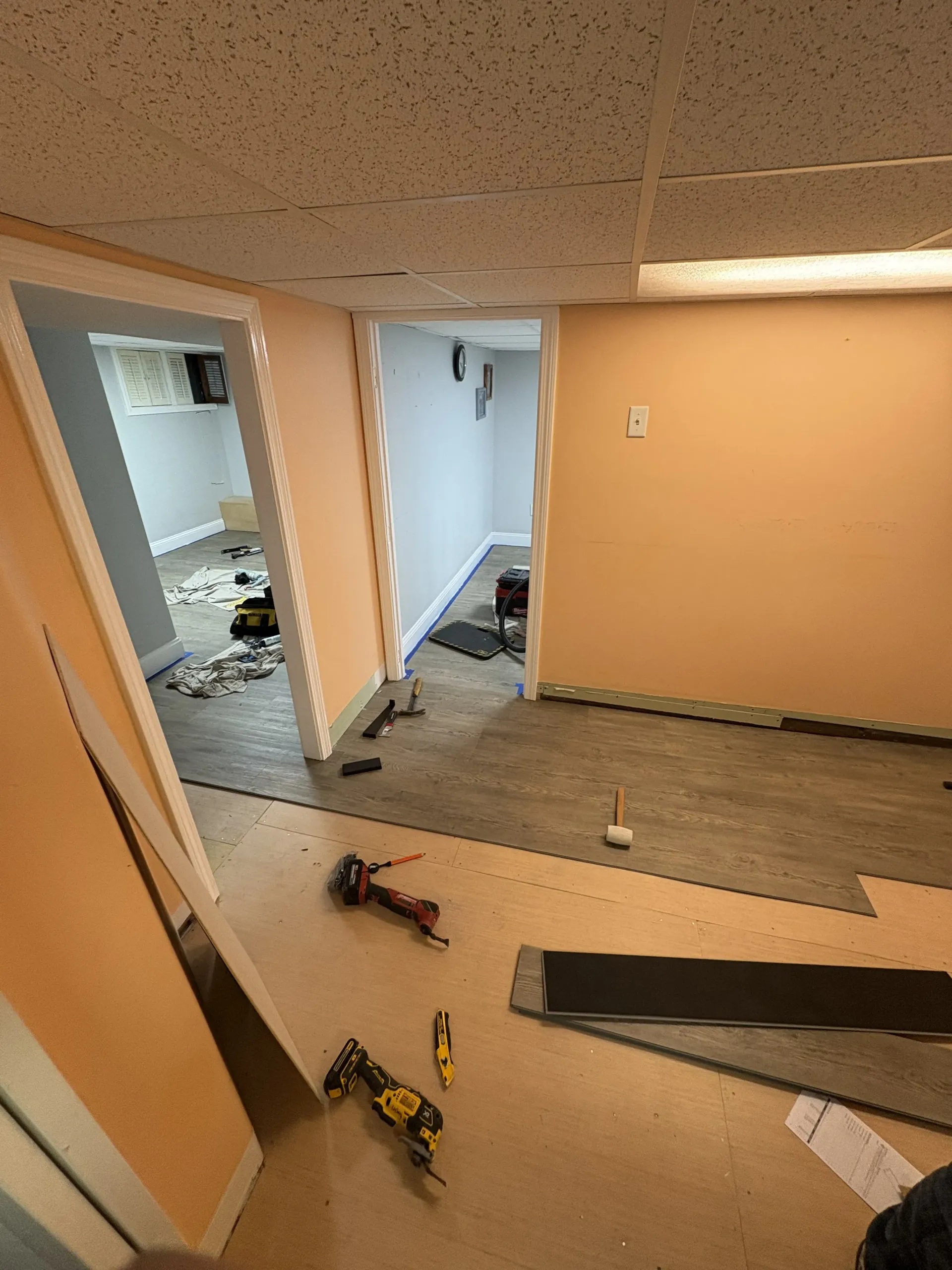 Basement remodel with torn-up carpet, tools on floor, and exposed subfloor in a hallway