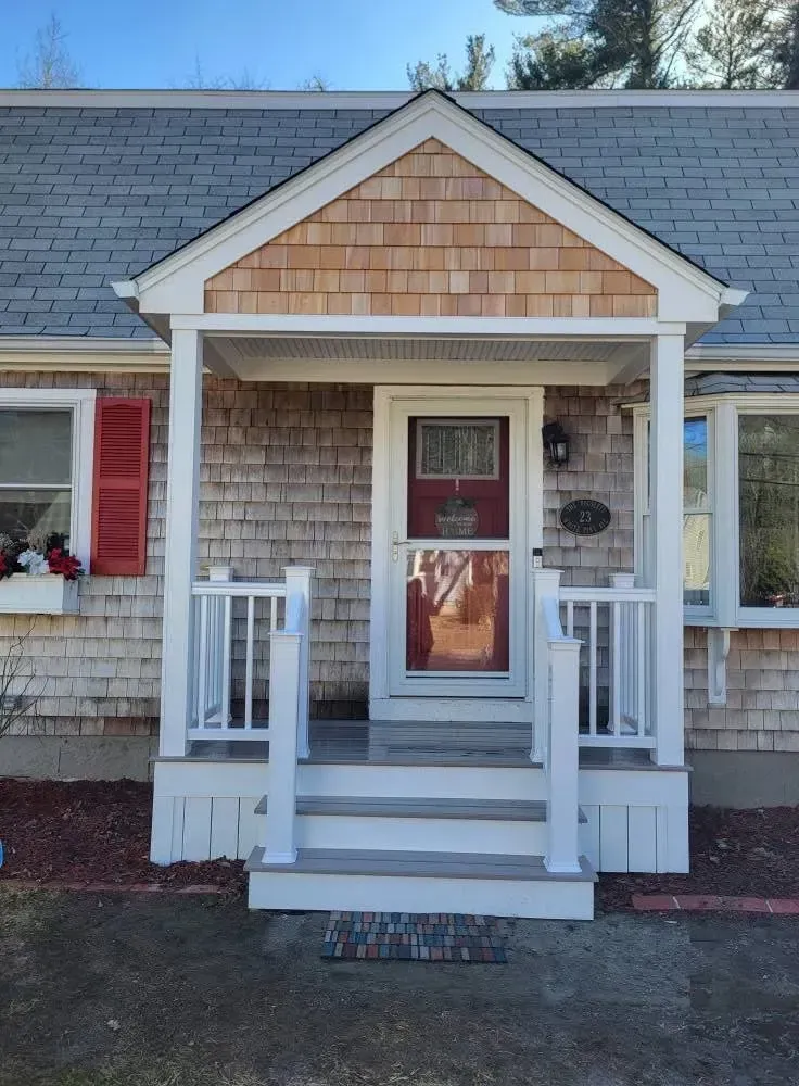 Front porch with white railings and steps leading to a red door on a shingled house.