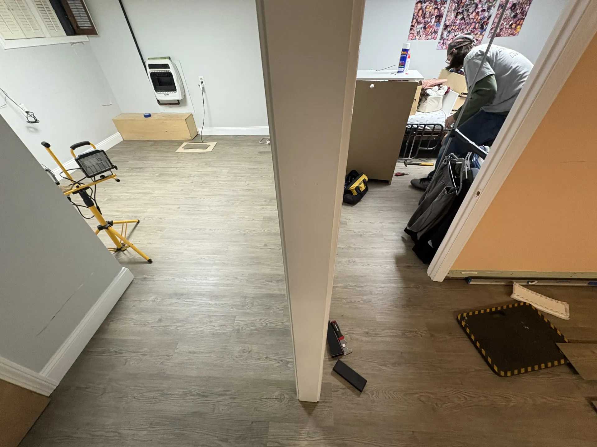 Basement renovation with tools and materials; worker kneeling near a cabinet on the right.