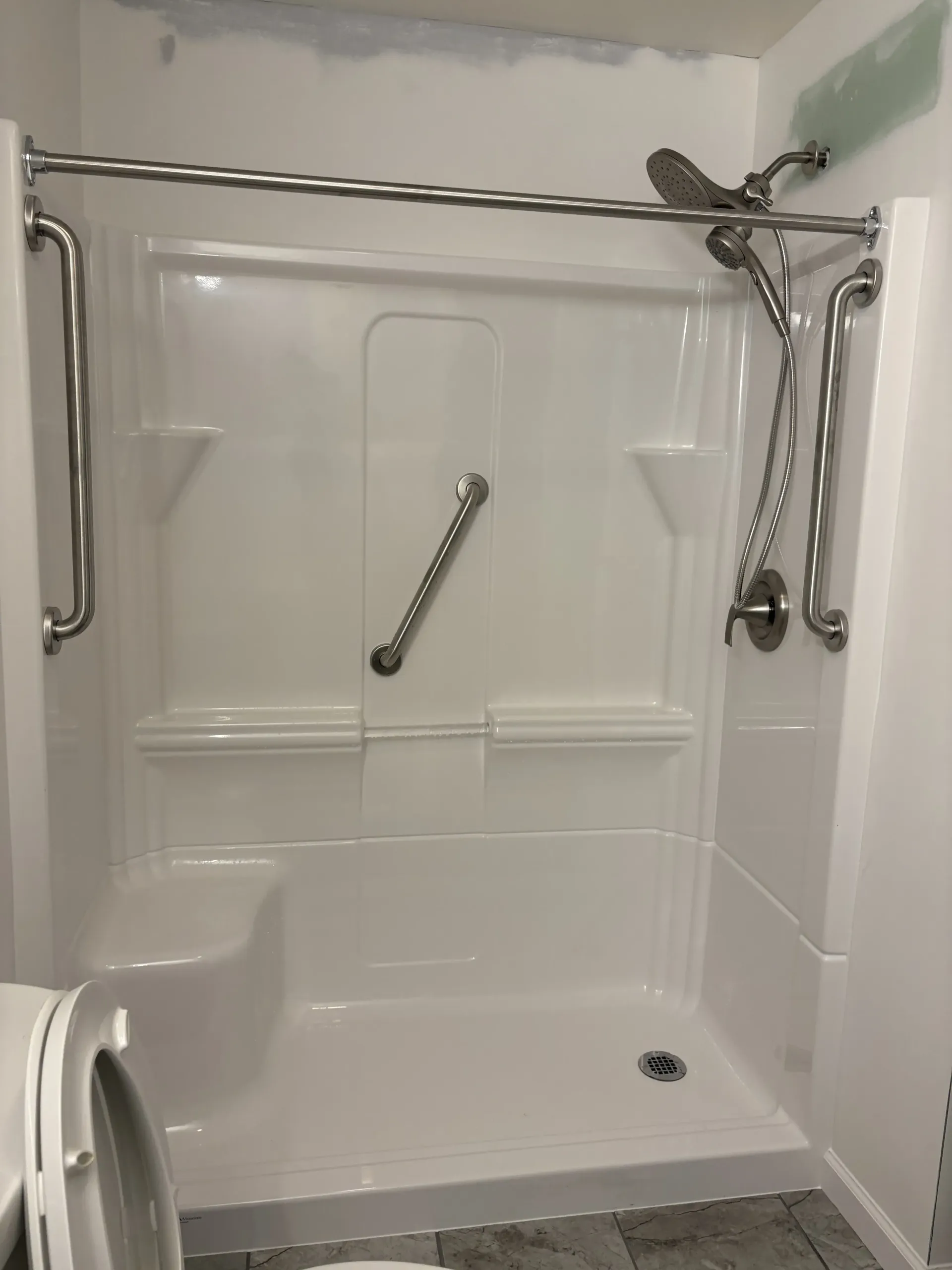 White accessible shower stall with grab bars, fold-down bench, and handheld shower head
