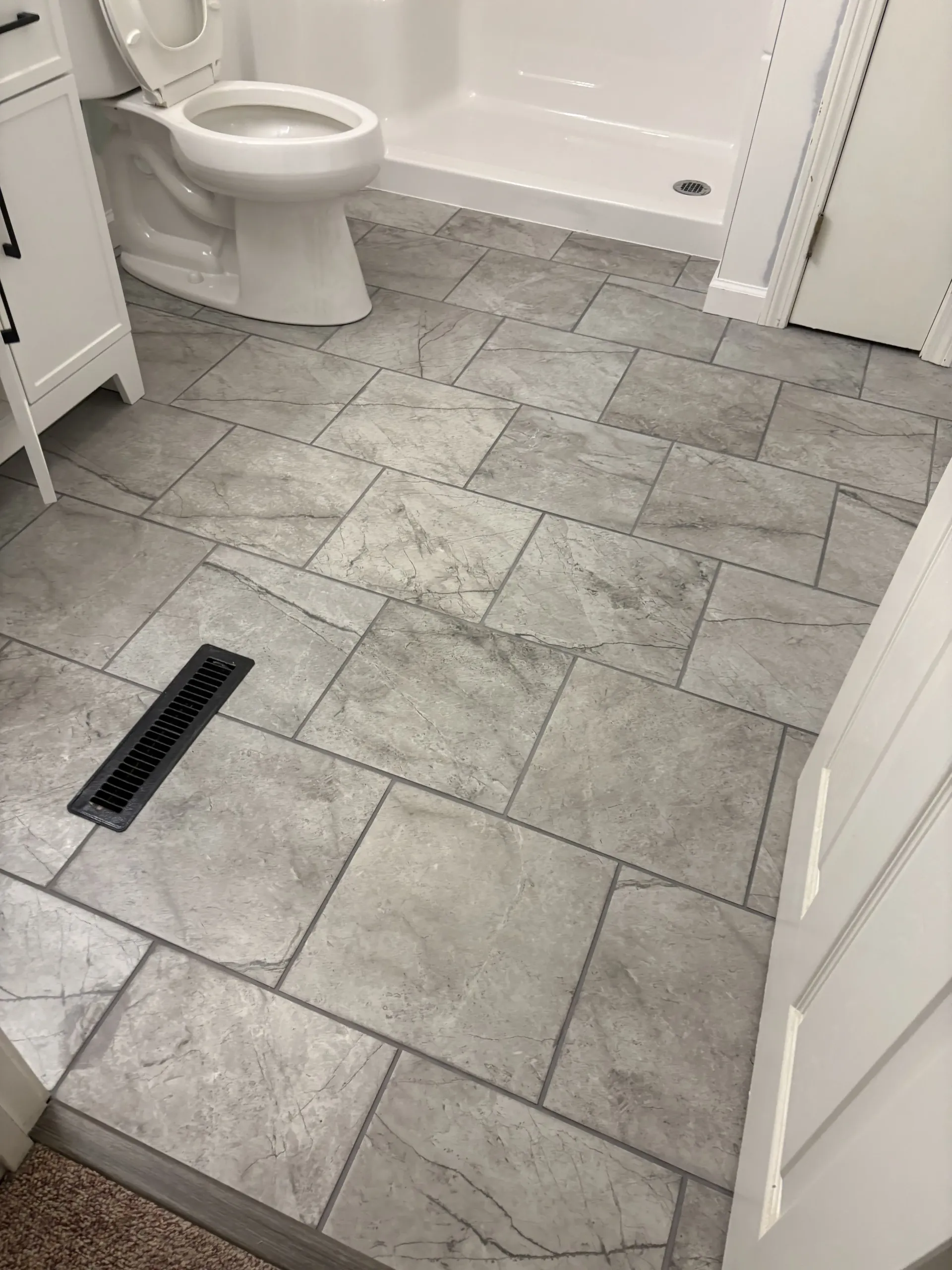 Bathroom with gray tiled floor, toilet, bathtub, and floor drain near the doorway