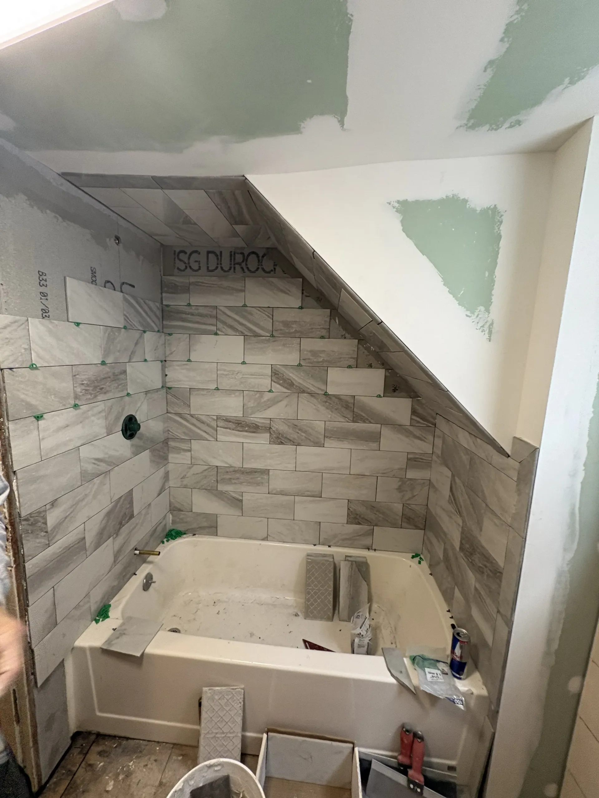 Tiled bathroom shower under construction with white wall panels and a bathtub base in place