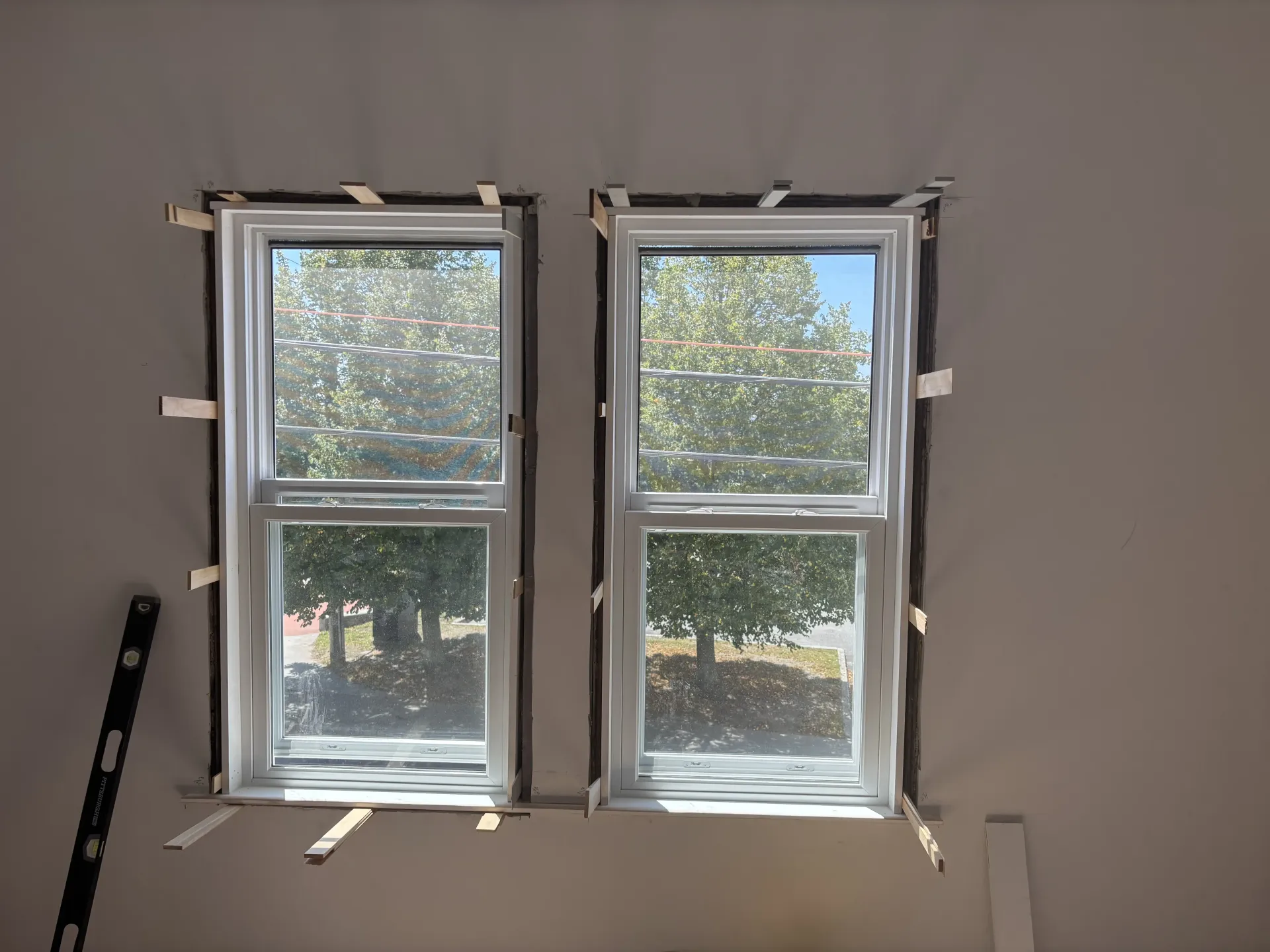 Two small windows set in a wall opening during construction, with tape and trim around the frames.
