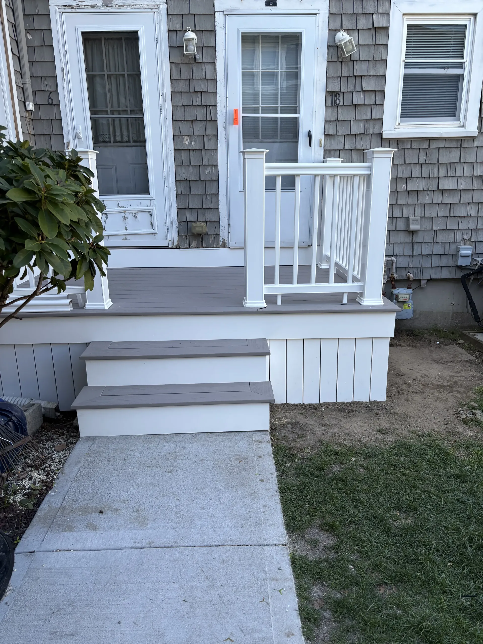 Small front porch with steps, white railing, gray house siding, and a concrete walkway.