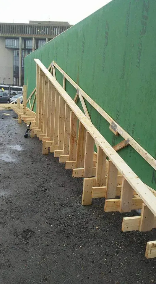 Wooden braces leaning against a tall green wall along a construction walkway