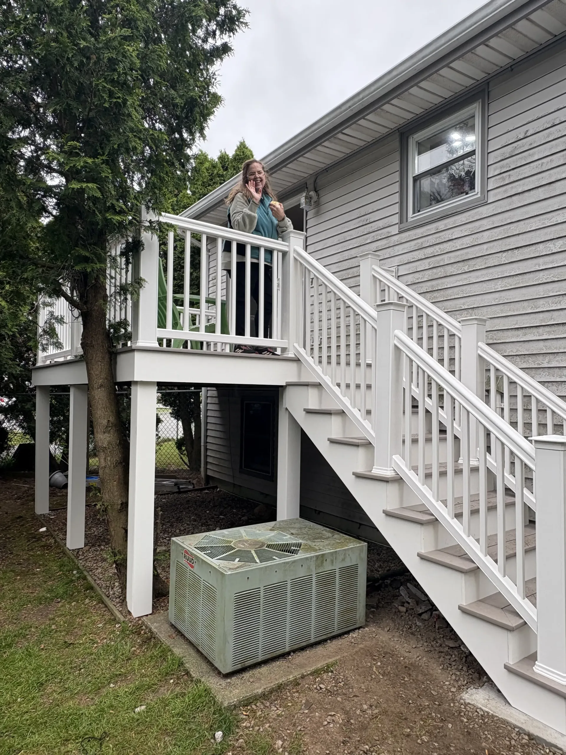 Person on an elevated wooden deck beside a house, with stairs and a large crate below.