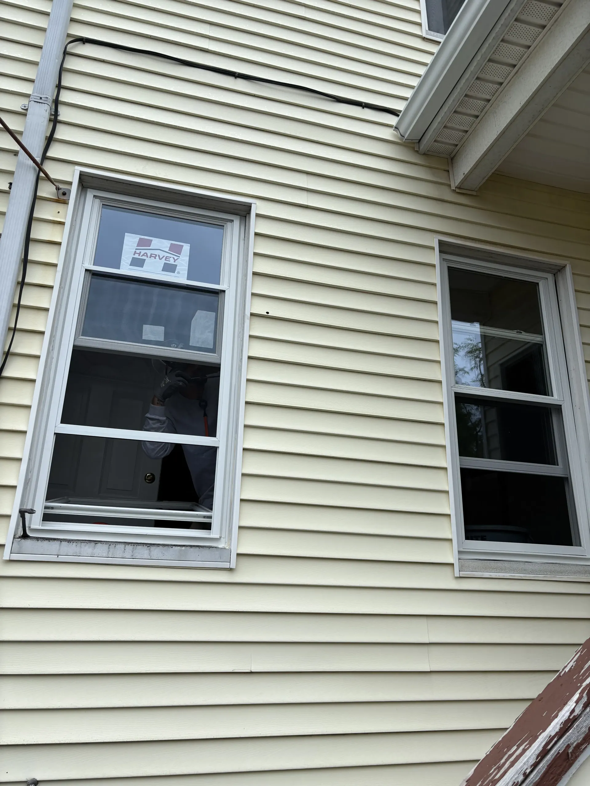 Two broken windows on a beige house exterior with white trim and horizontal siding
