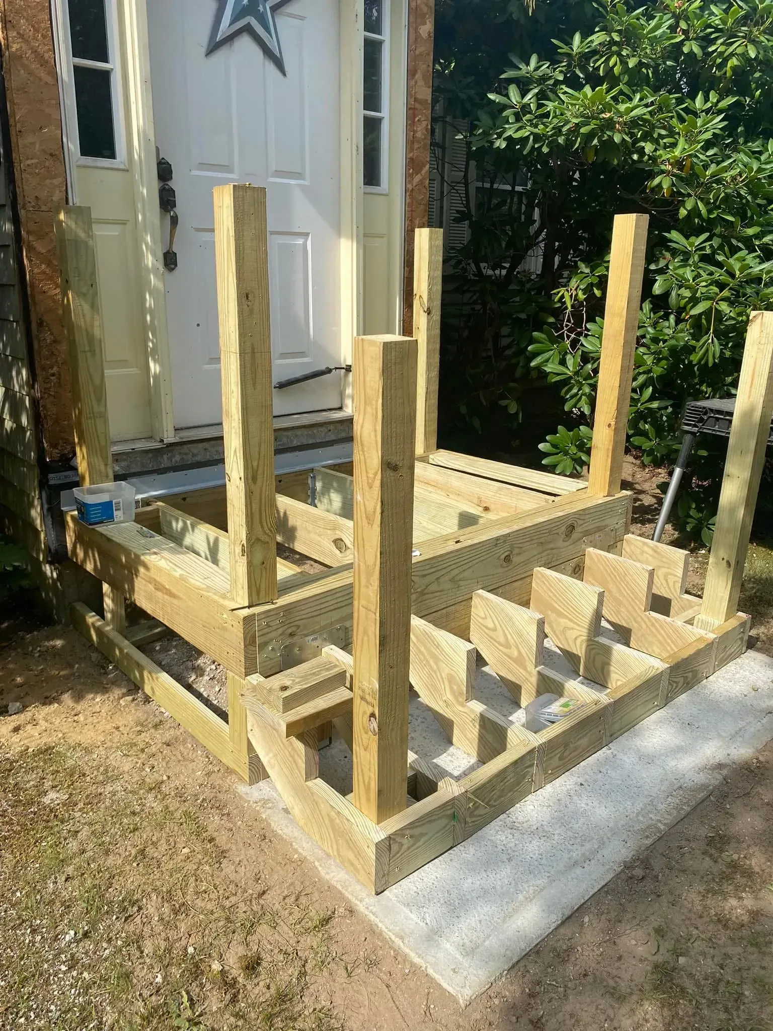 Partially built wooden deck frame with posts beside a house and a concrete step in a yard