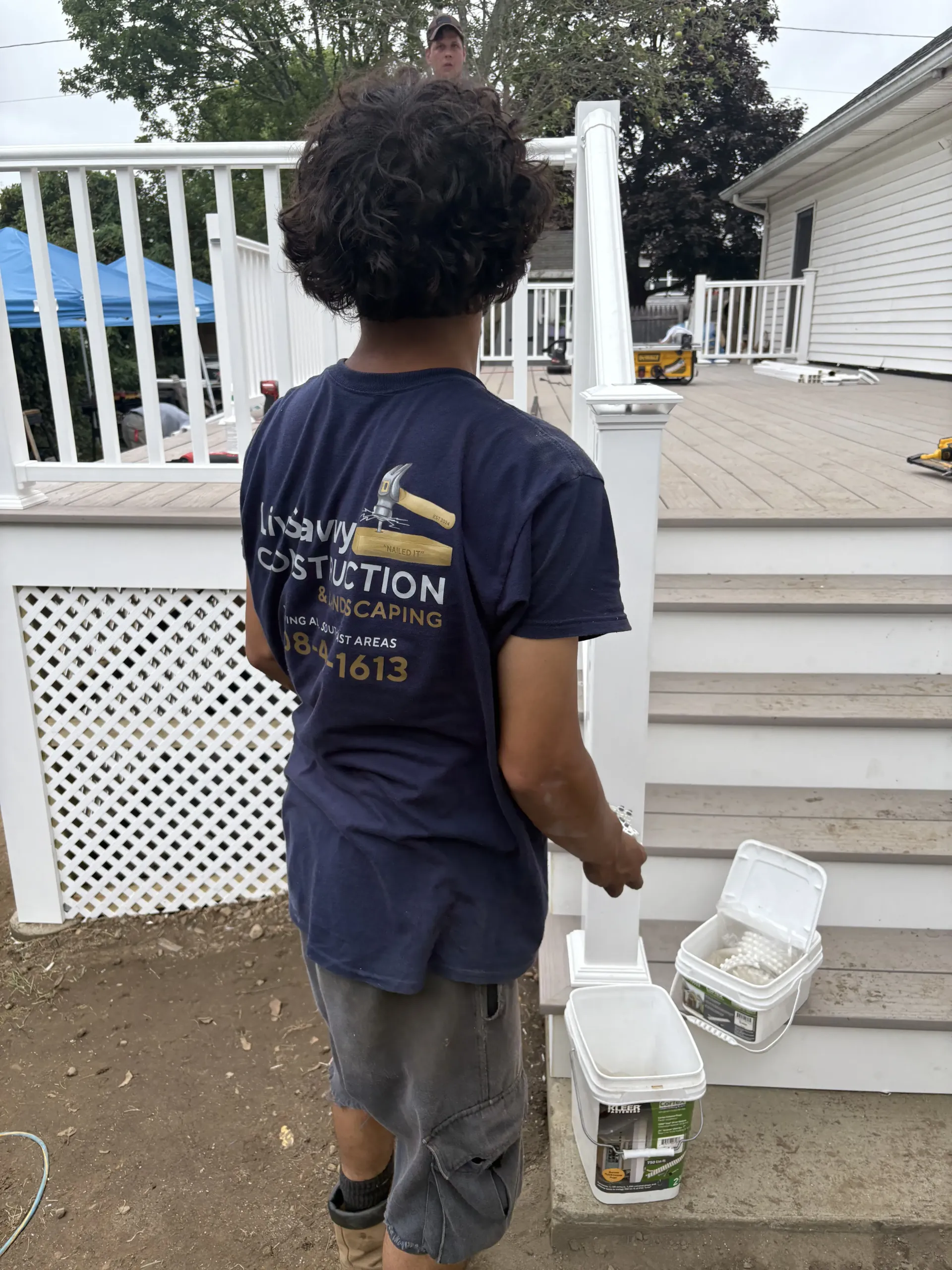 Child walking on a porch holding white plastic containers, with a house and railing in the background.
