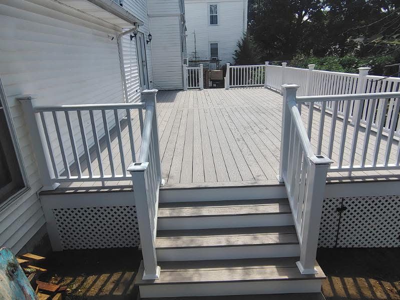 Wooden deck stairs with white railings leading to a fenced outdoor patio