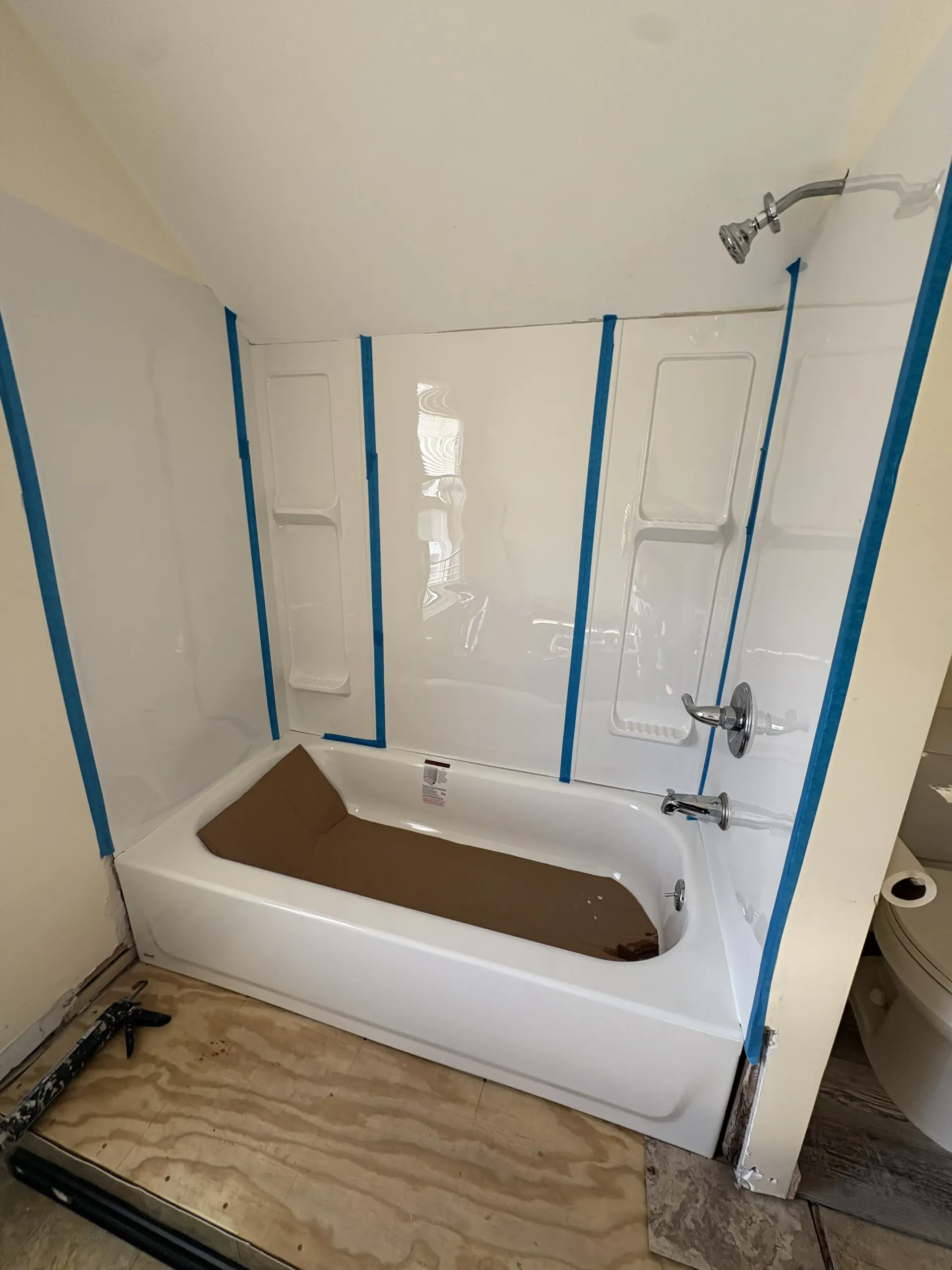 Bathroom under renovation with a white bathtub, blue painter’s tape, and unfinished flooring.