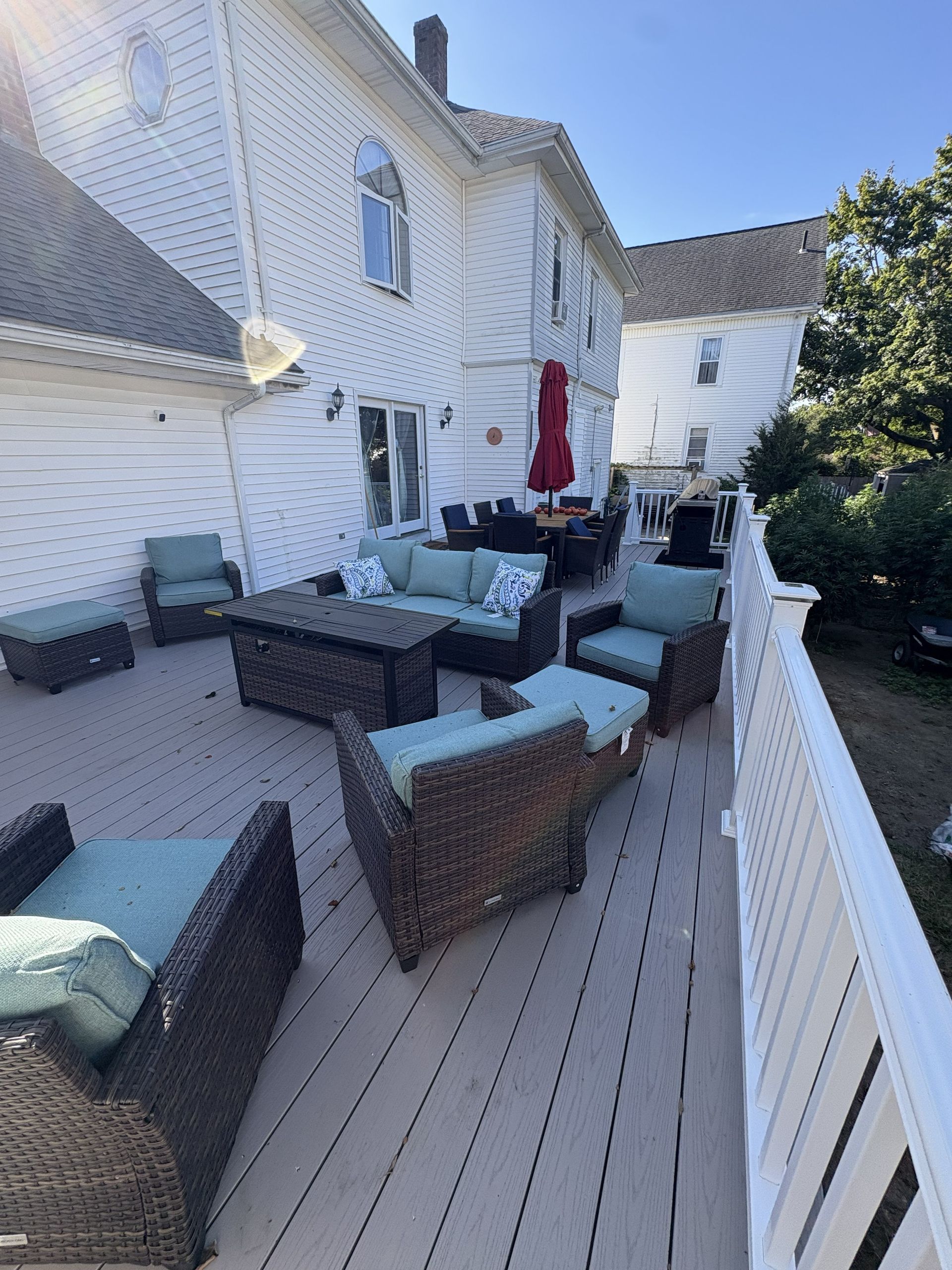 White house deck with wicker patio furniture, teal cushions, and a red umbrella in bright sunlight
