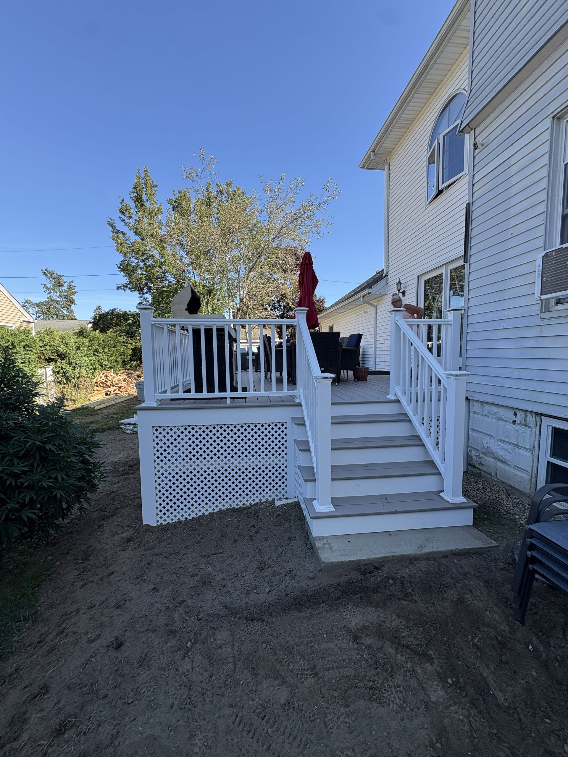 White porch stairs with railings beside a white house, leading up from a dirt yard under a clear blue sky